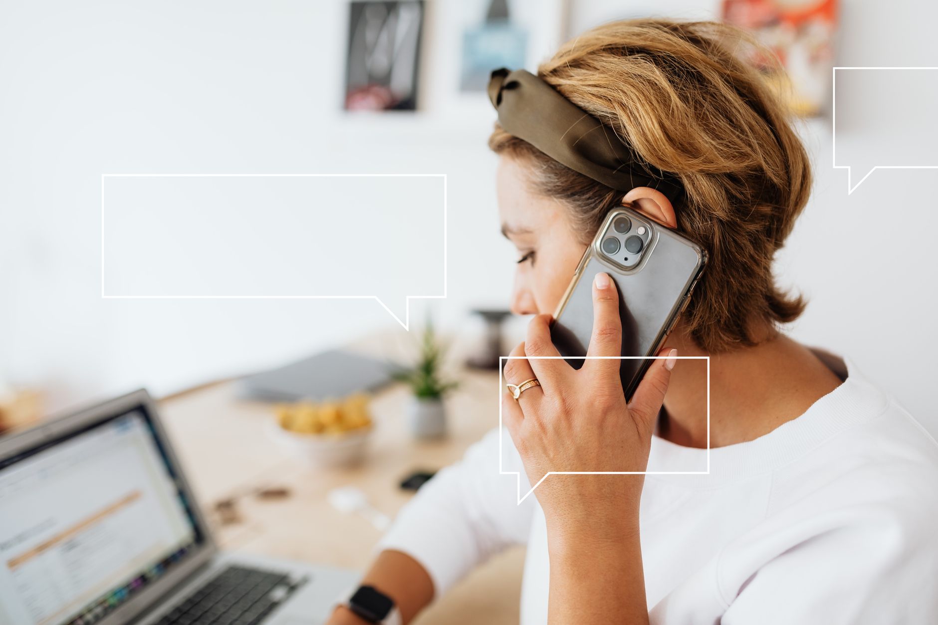 A woman multitasking, on a phone call while working from home with a laptop.