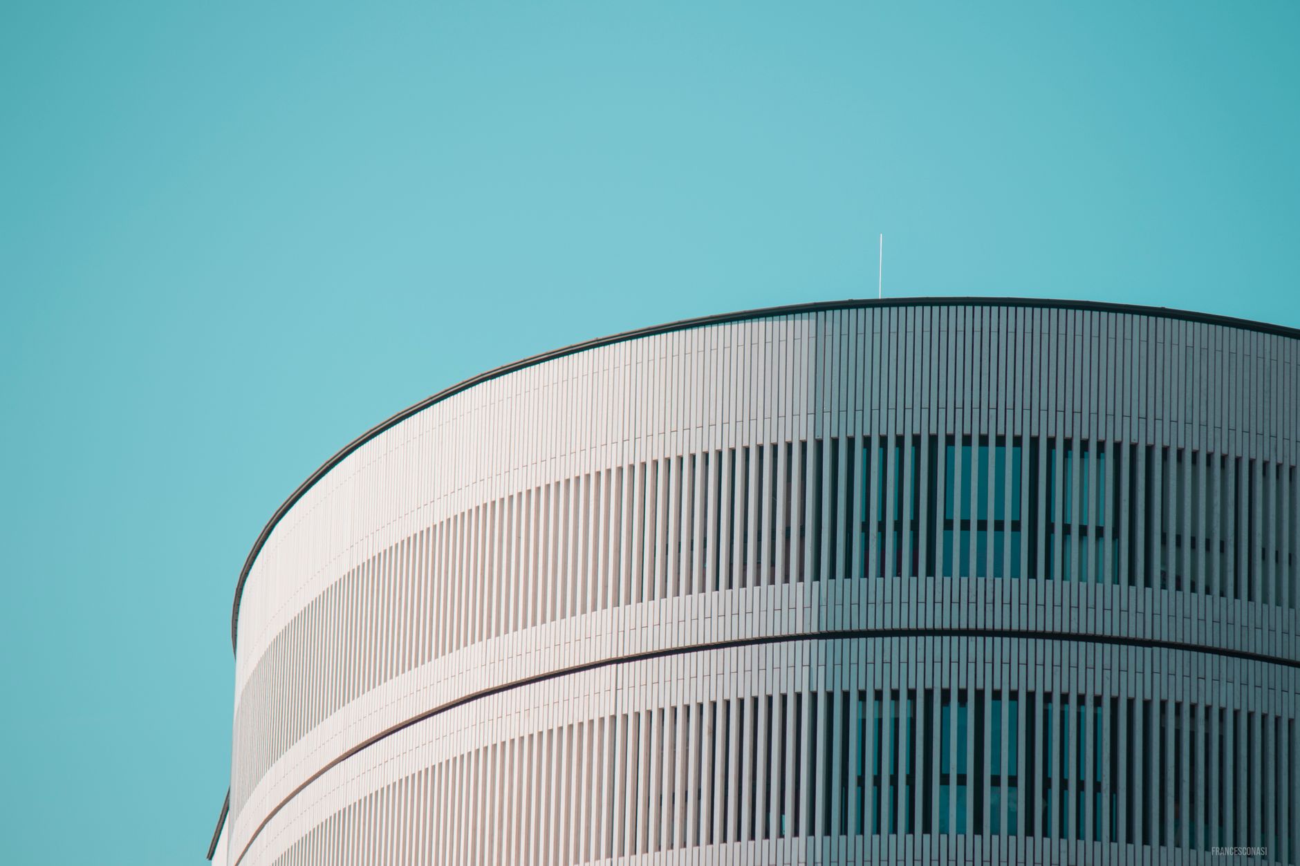 Striking modern cylindrical building with sleek design against a clear blue sky in Milan, Italy.