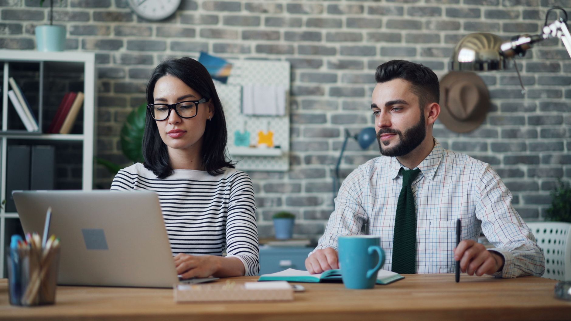 Two professionals collaborating at a desk with a laptop, in a modern office setting.