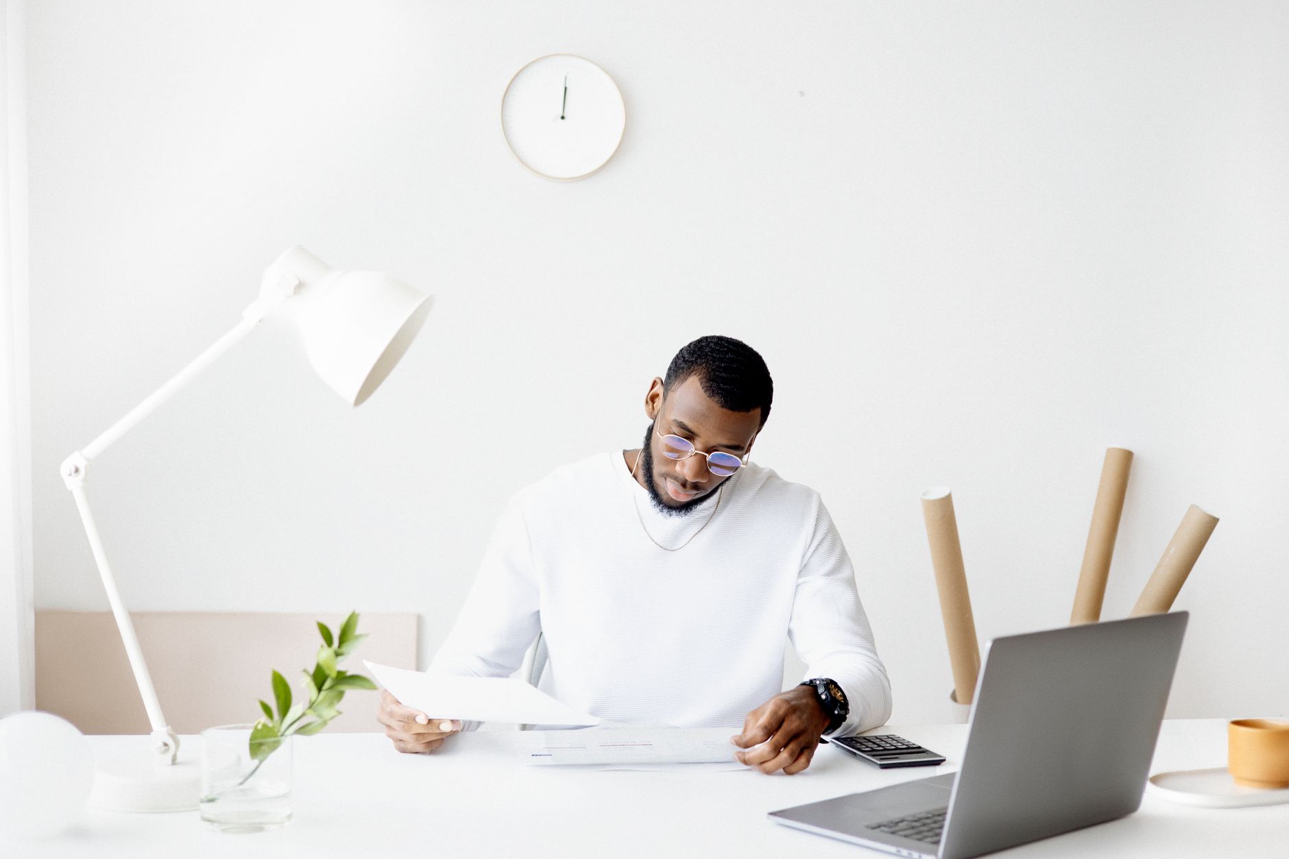 A professional adult working intently at a minimalist desk with a laptop, papers, and a lamp.