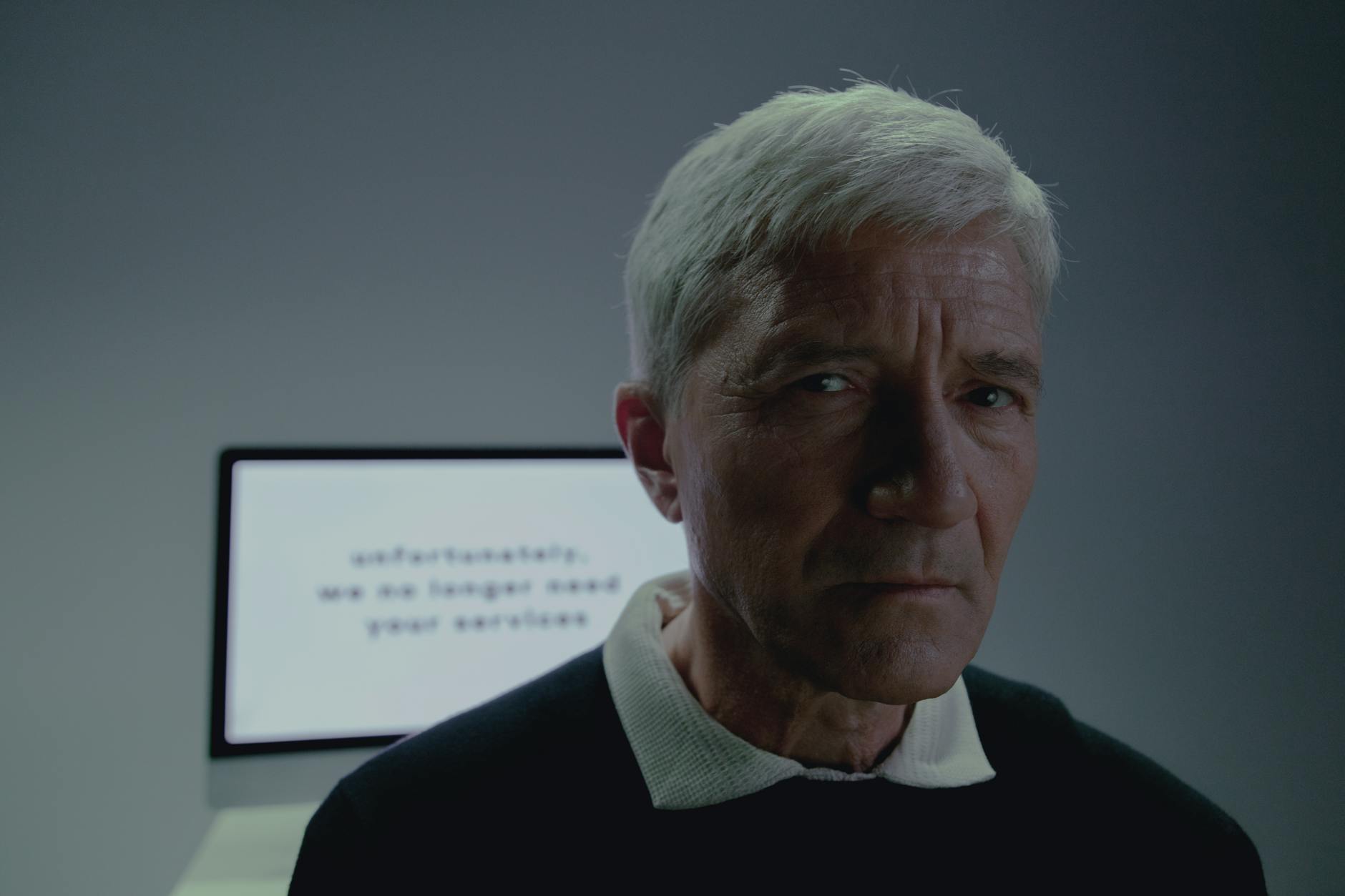 Elderly man looking thoughtful after reading a termination notification on screen.