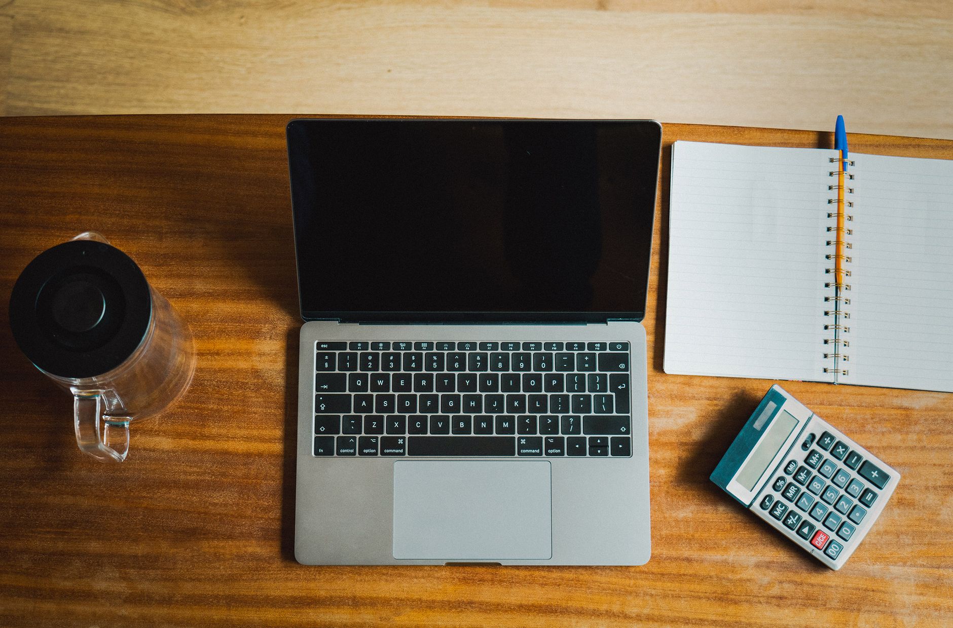Flat lay of workspace featuring a laptop, calculator, and notebook on a wooden desk.