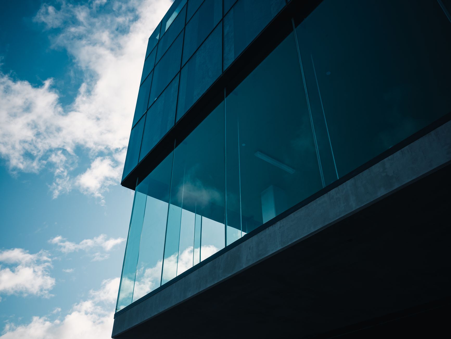 Low angle view of modern glass building against a vibrant blue sky with clouds.