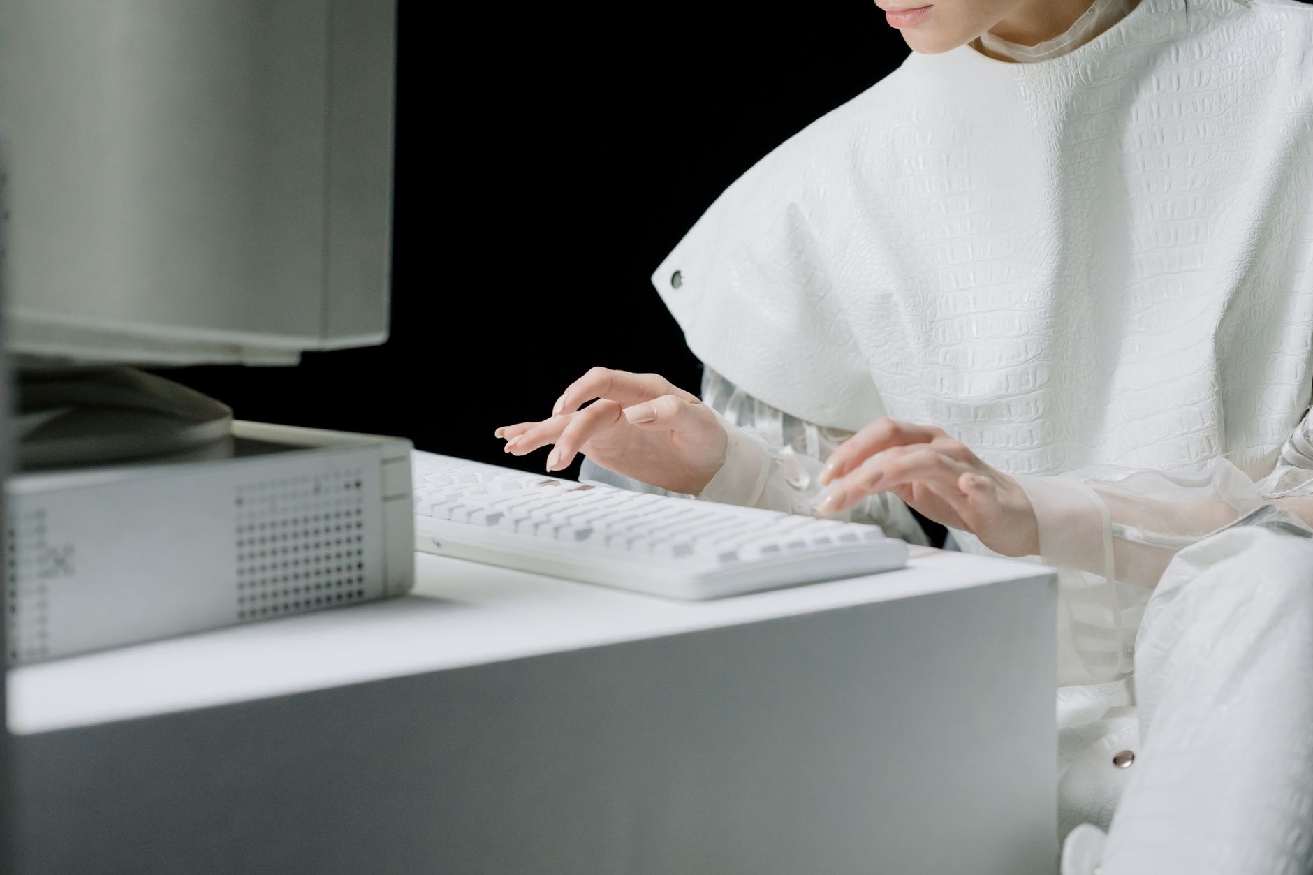 A woman in a white outfit typing on a white keyboard in a modern setting.