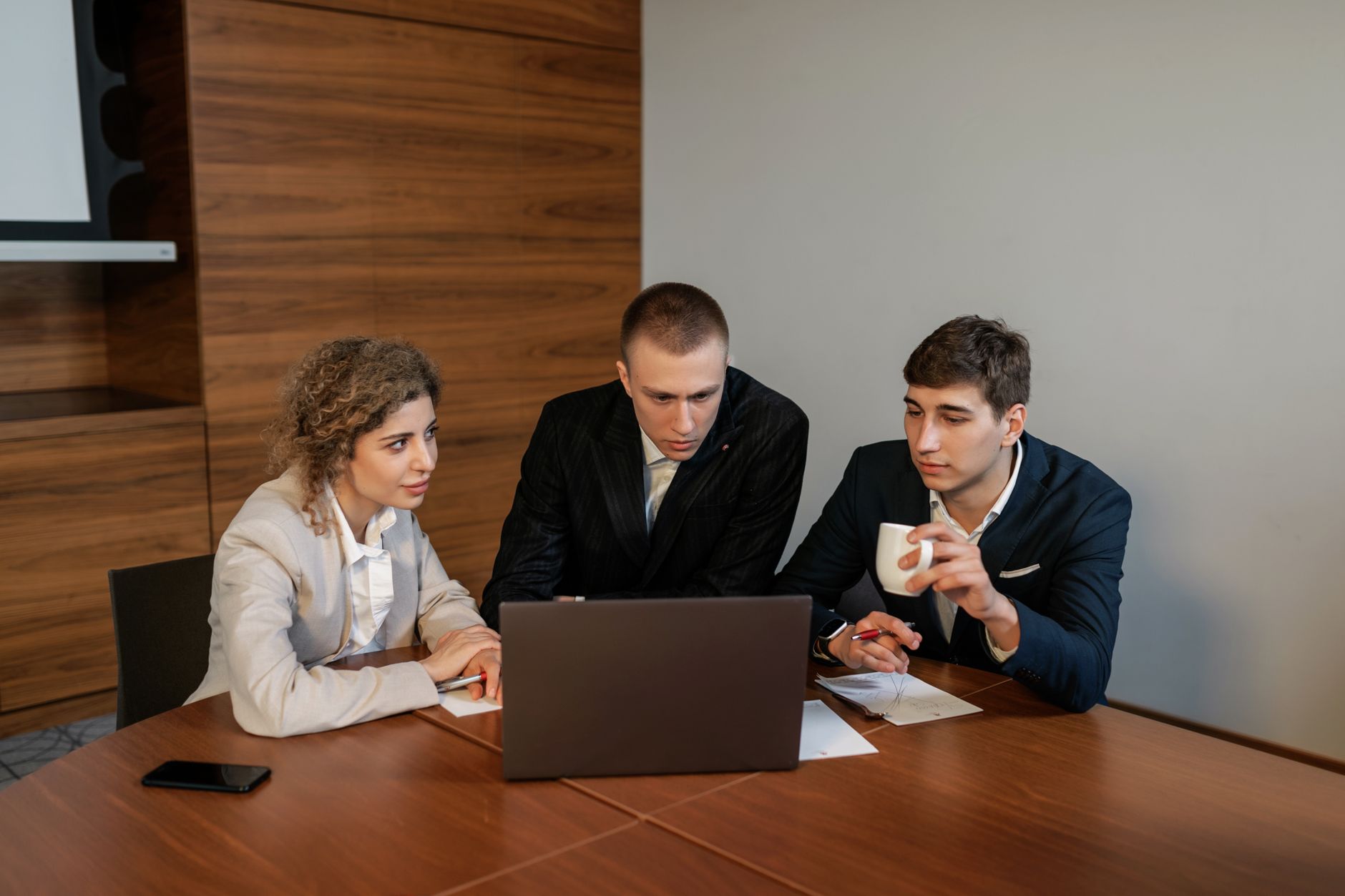 Three professionals collaborate in a modern office setting focused on a laptop.