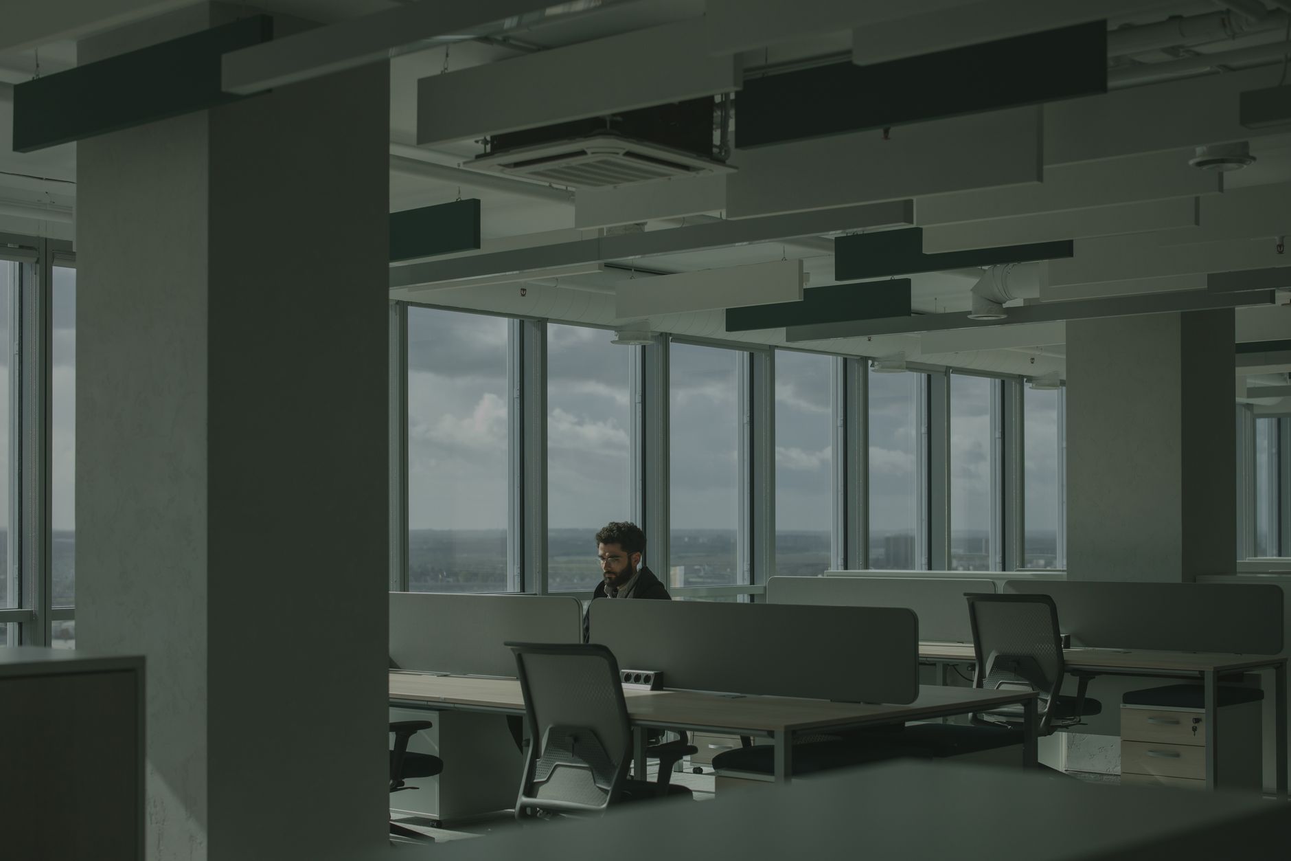 A man works alone in a spacious, modern office with large windows and natural light.