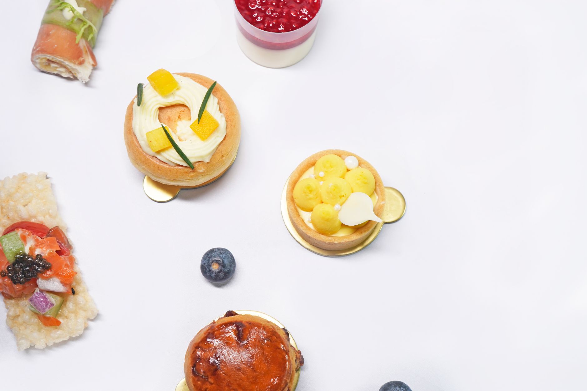 Artistic flat lay of gourmet desserts including pastries and fruit tarts on a white surface.