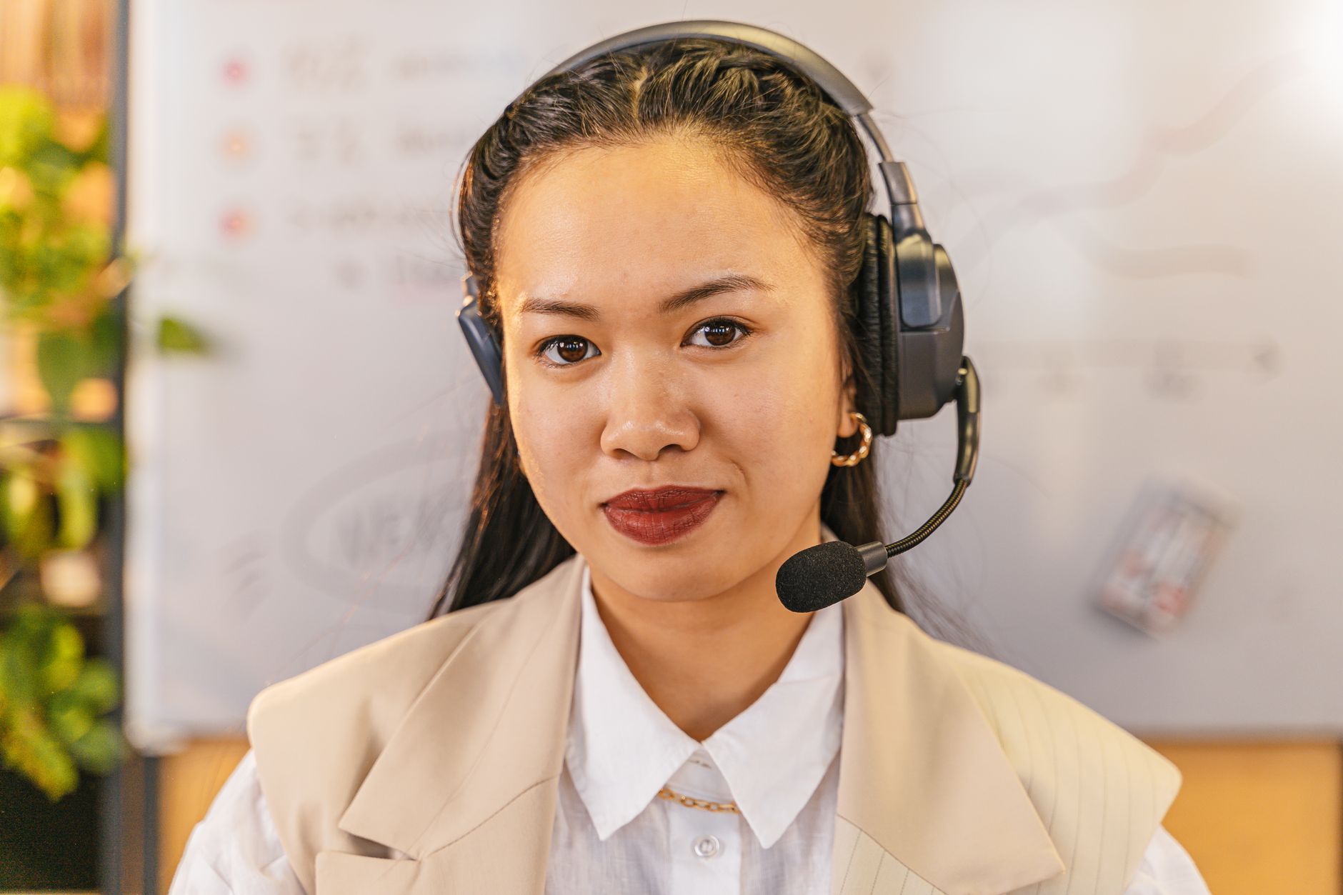 Professional Asian woman in headset smiling confidently in a modern office setting.