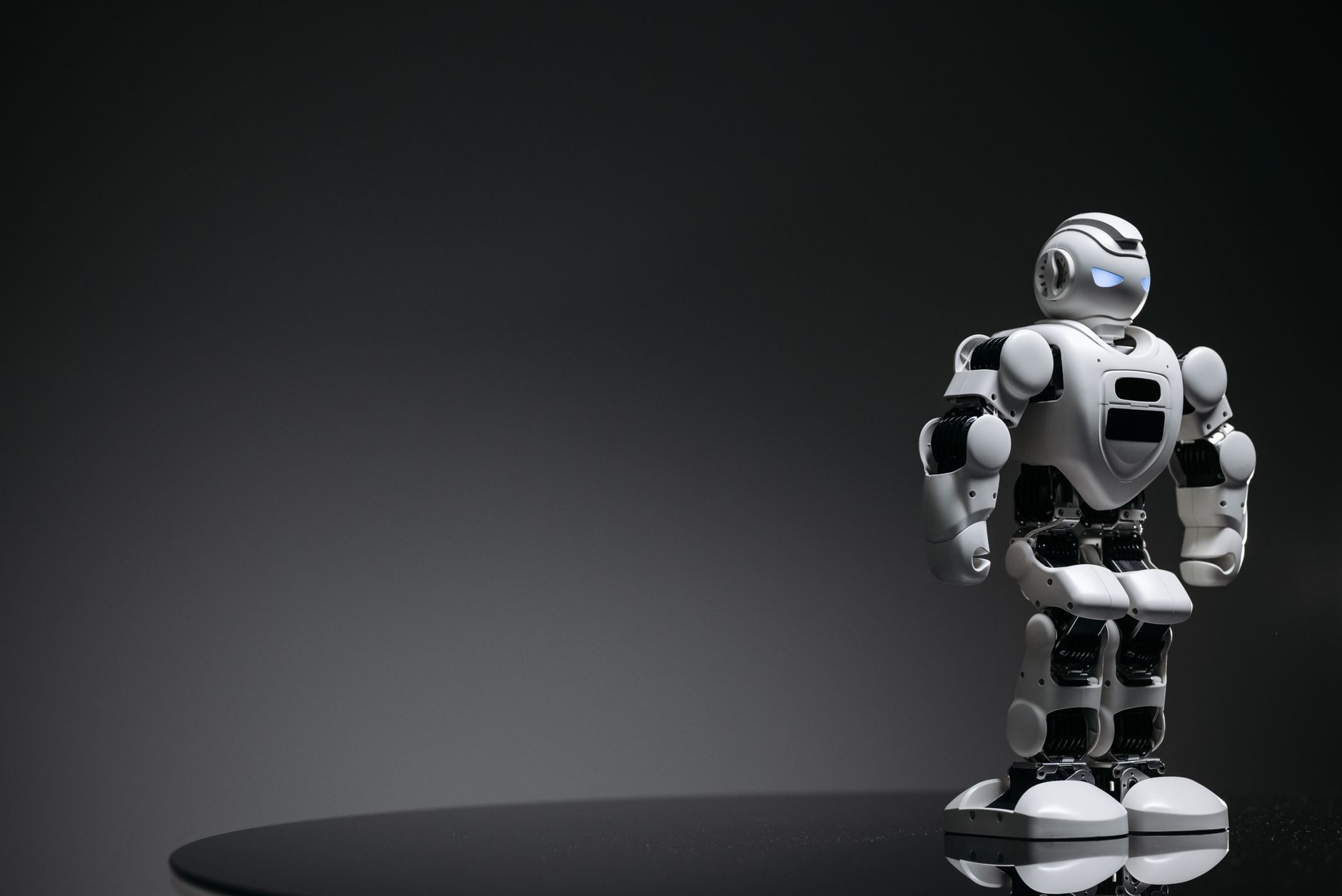 Compact humanoid robot toy standing on a reflective surface, exuding a futuristic vibe.