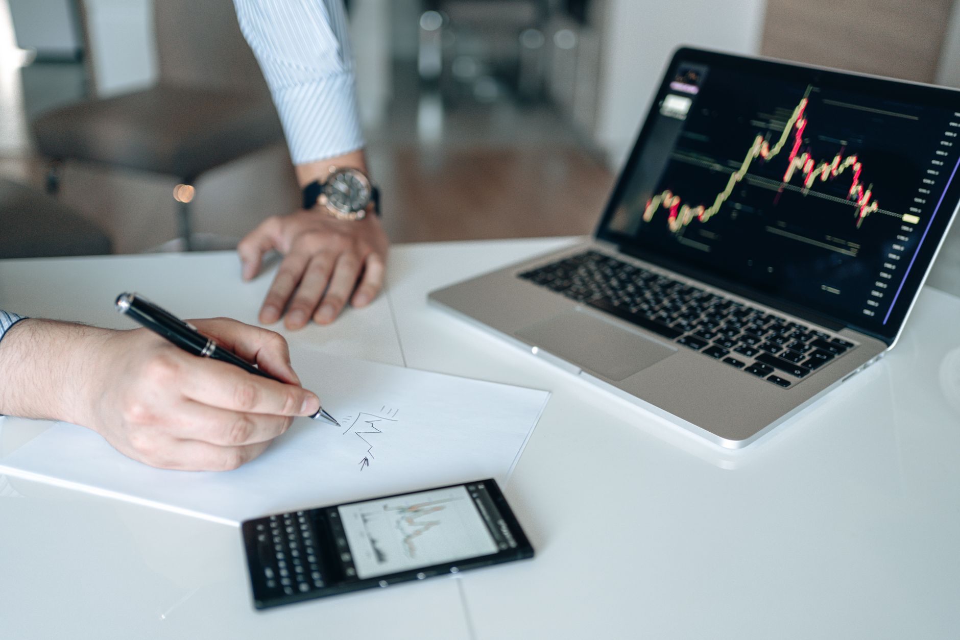 Professional workspace featuring laptop with stock charts, smartphone, and paper for business analysis.