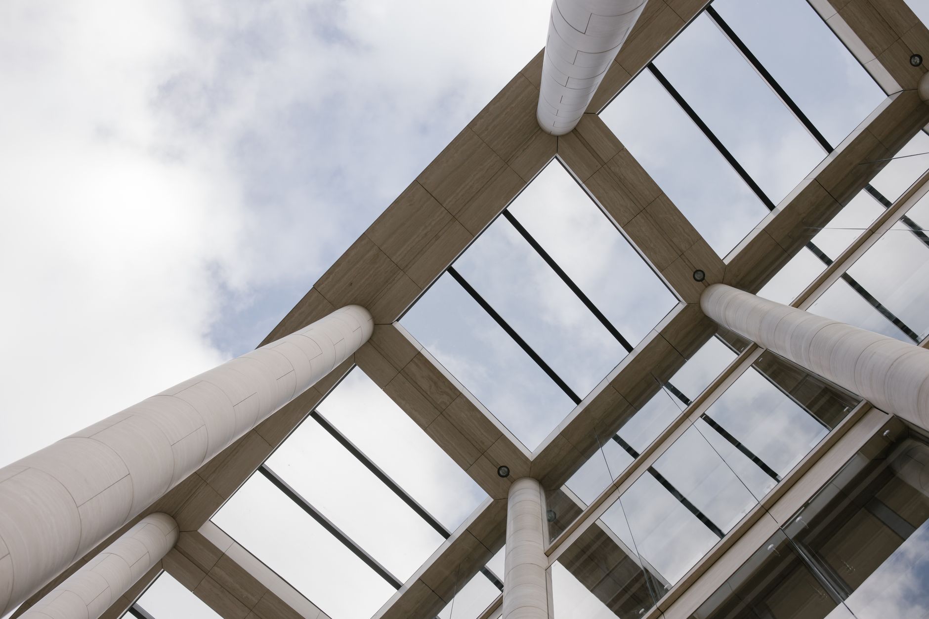 Upward view of modern architecture with tall concrete pillars and glass ceilings.