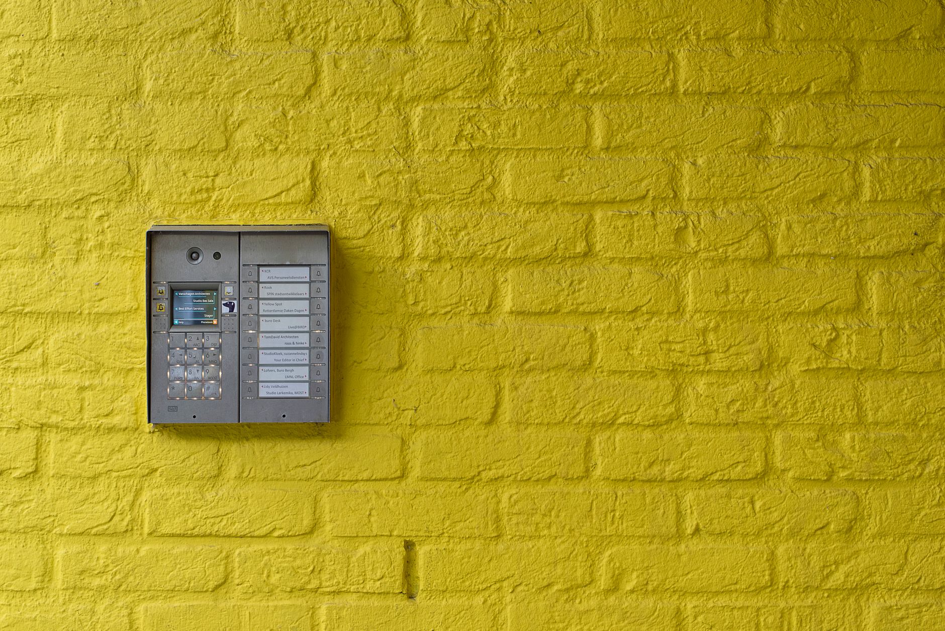 A vibrant yellow brick wall featuring a modern intercom system, ideal for security or design concepts.