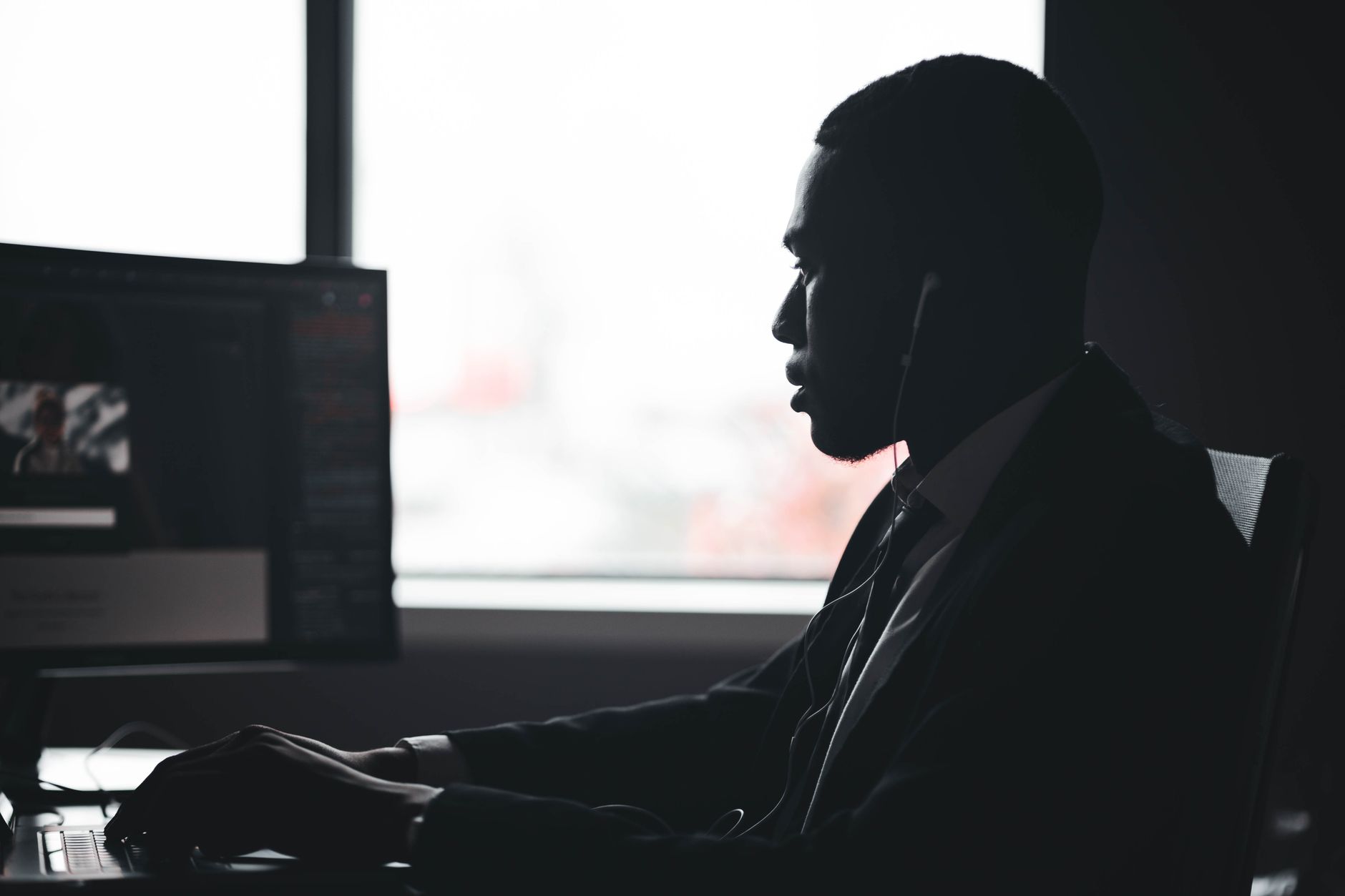 Silhouette of a man working at a computer desk in a modern office setting.