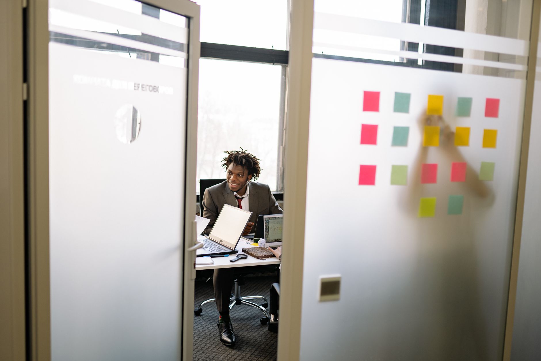 Businessman in office with laptops and sticky notes on glass wall during a meeting.