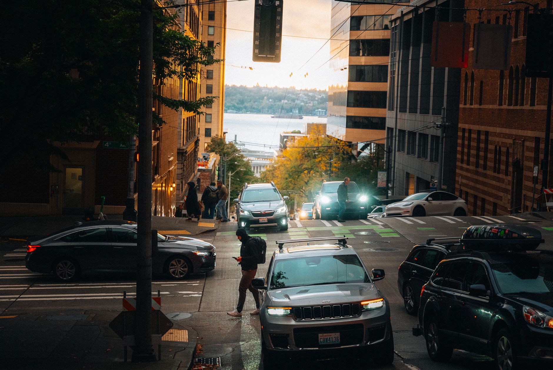 A bustling Seattle street scene at sunset showing cars and pedestrians with the bay in the background.