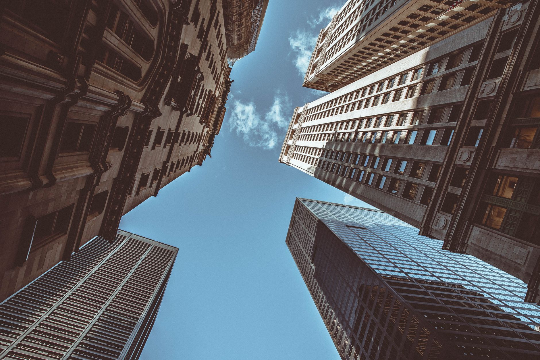 Upward perspective of New York skyscrapers against a clear blue sky, showcasing urban architecture.