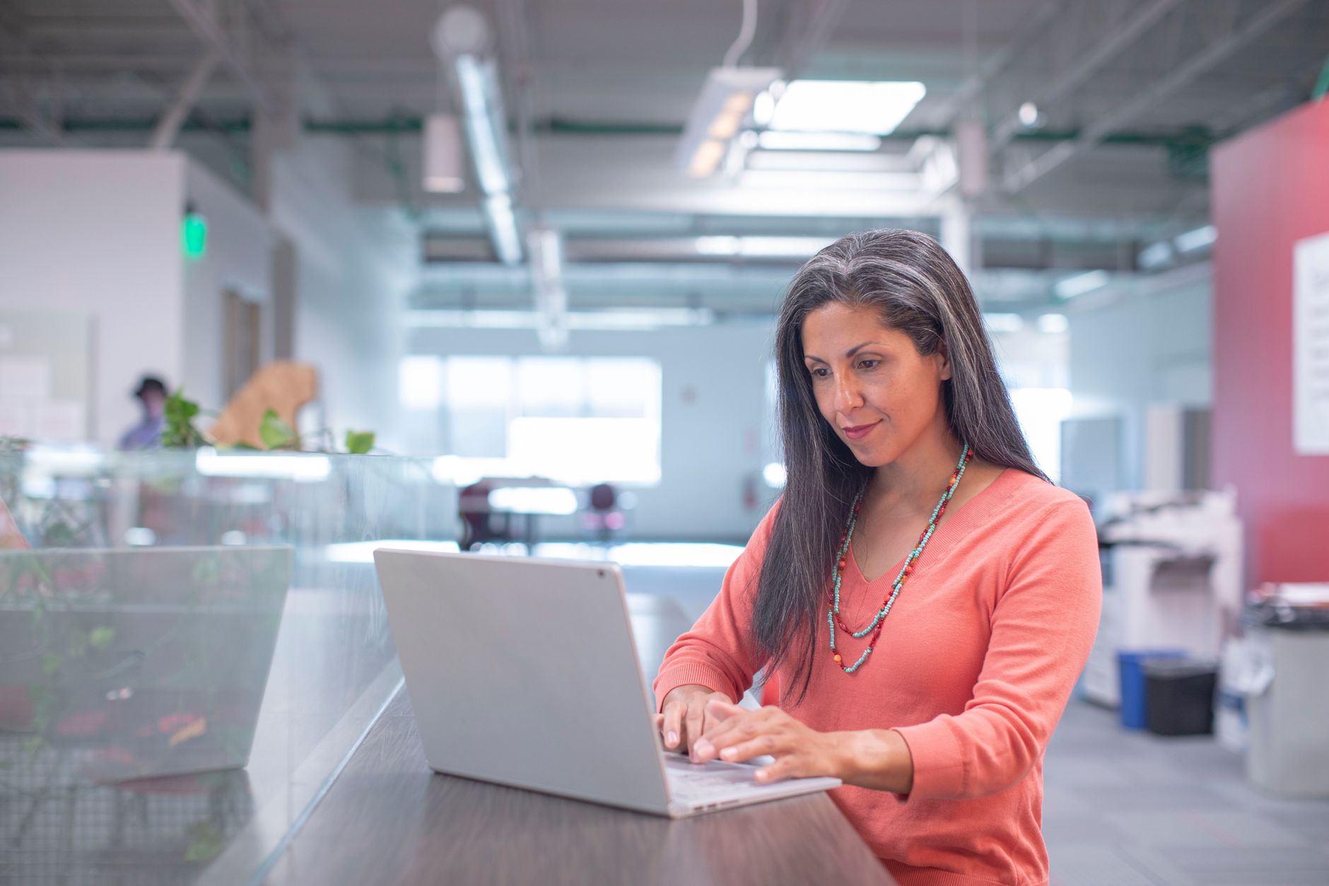 Professional woman typing on laptop in bright modern office environment.
