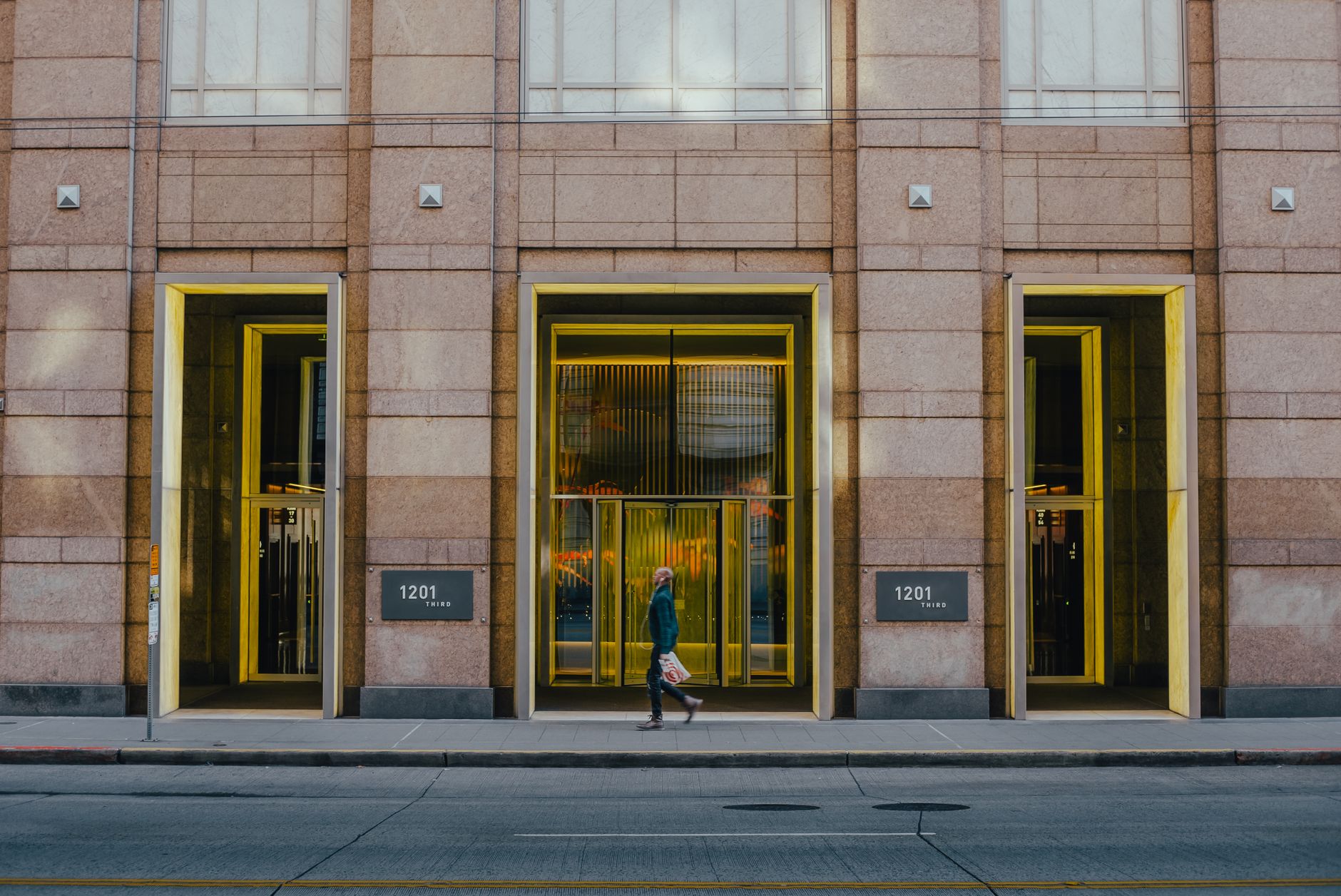 A modern city street scene featuring a building's architectural facade with illuminated doorways.