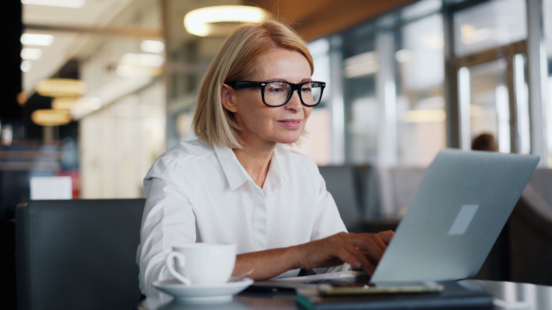 Focused woman with glasses using a laptop in a contemporary cafe.