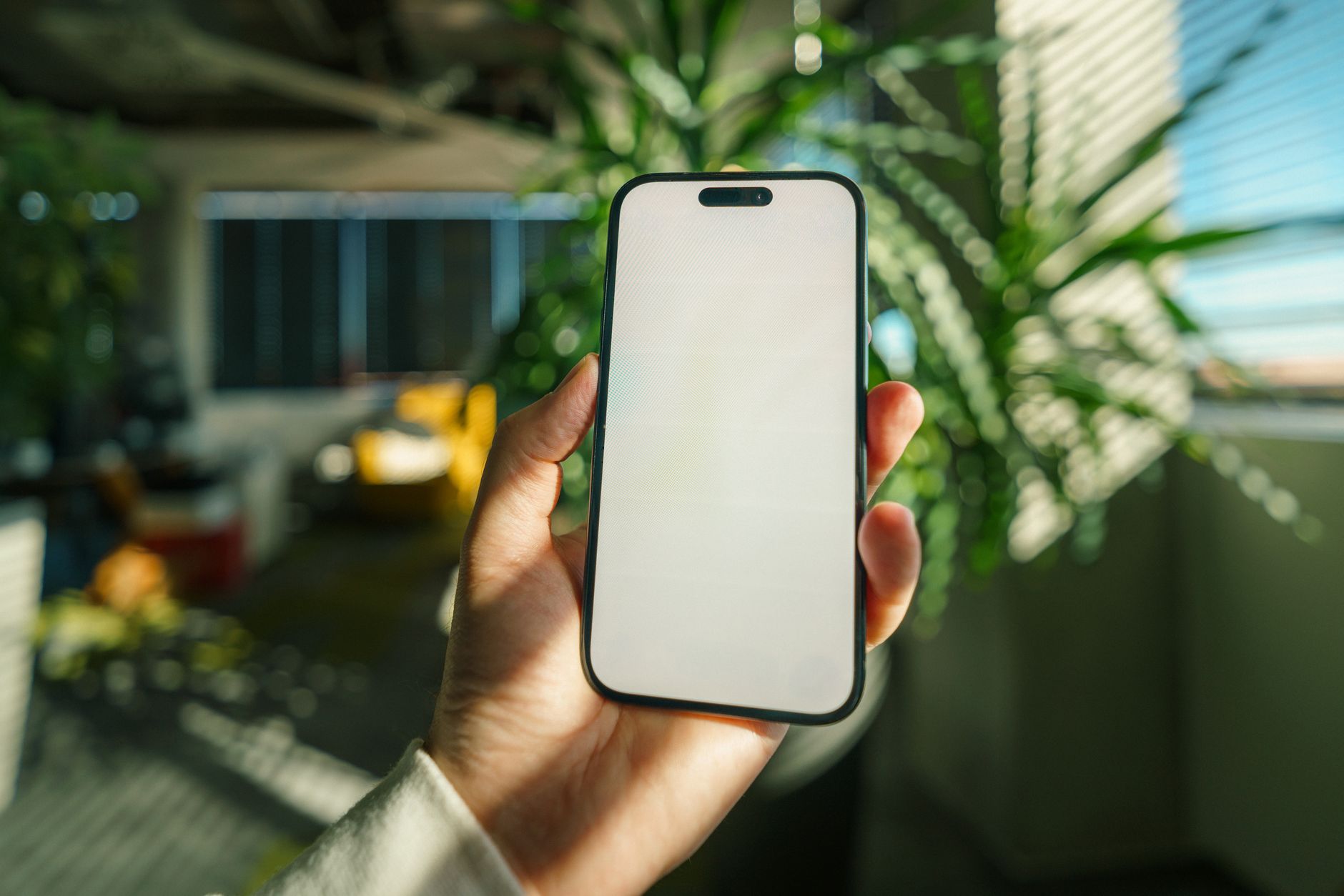 A hand holding a smartphone with a blank screen, surrounded by indoor plants, providing a fresh, modern aesthetic.