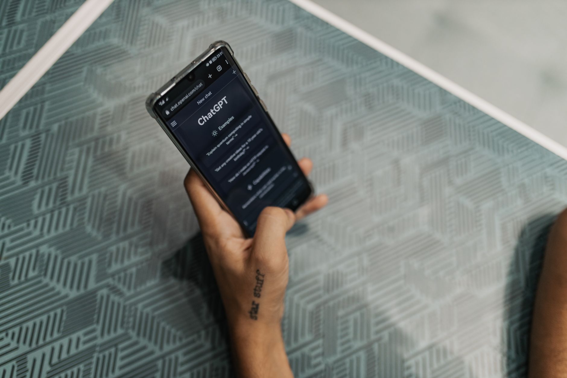 Close-up of a person holding a smartphone displaying the ChatGPT application interface on a patterned table.