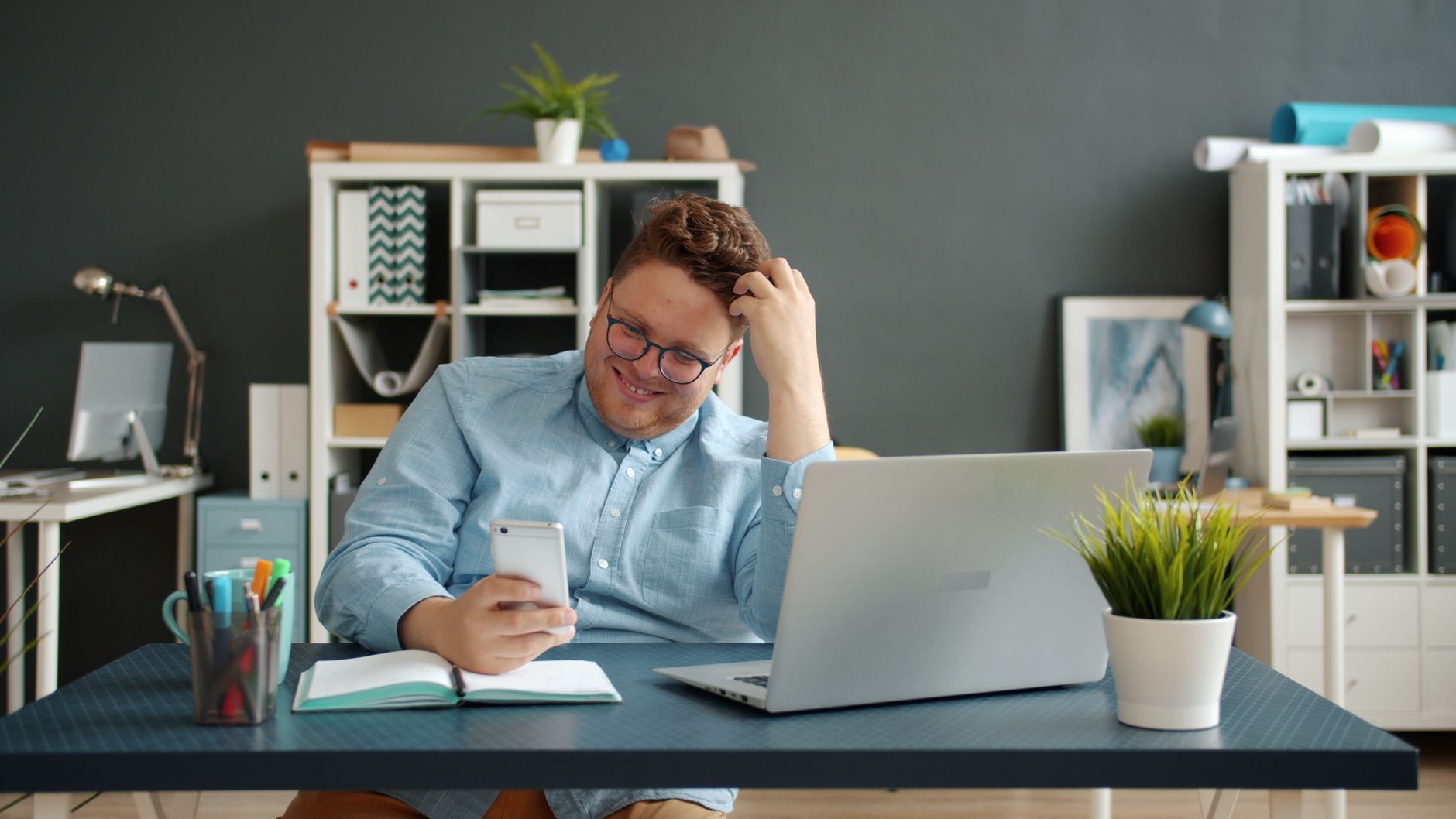 Smiling man in office using smartphone, engaged and relaxed.