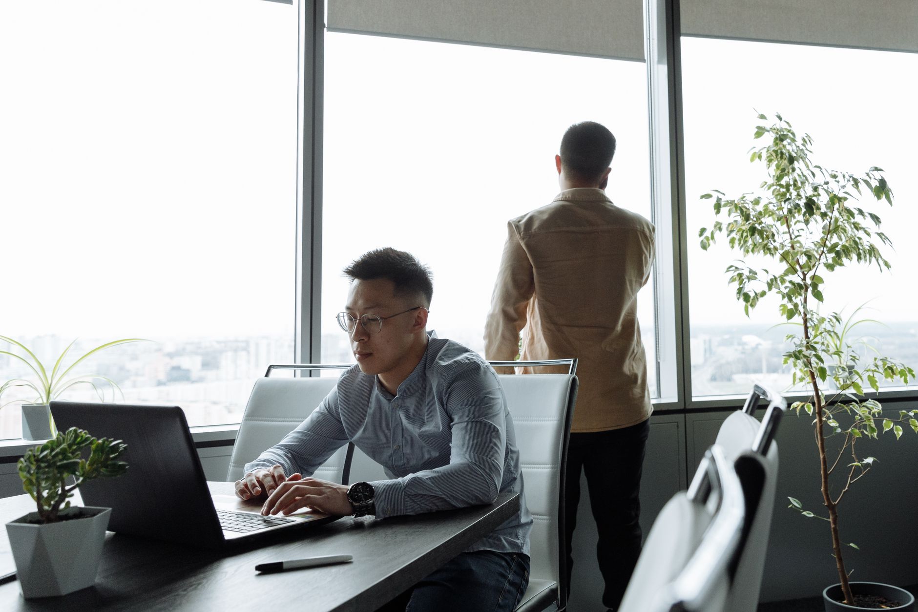 Two men working in a modern office with large windows and city view.