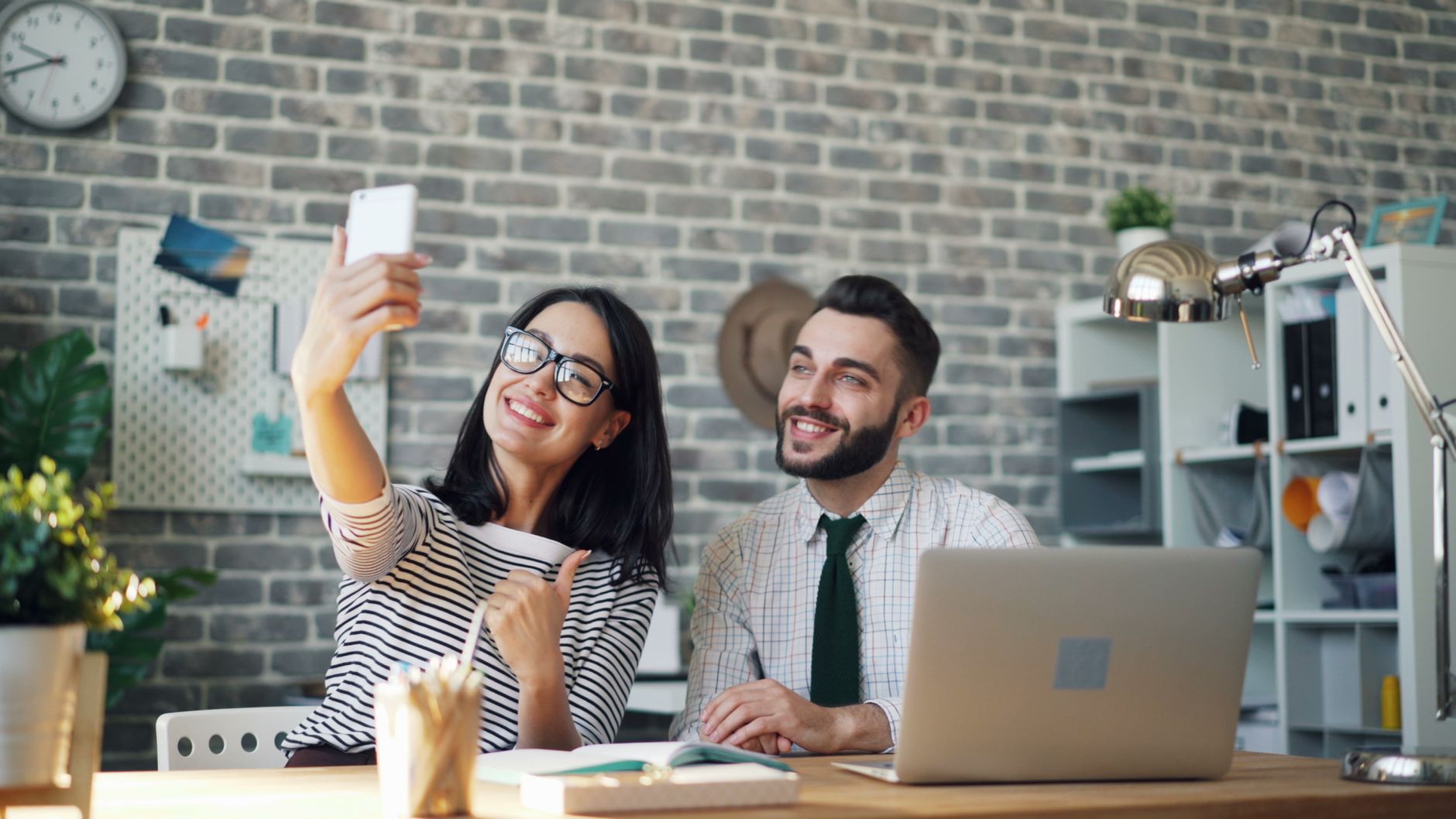 Smiling colleagues capturing a fun selfie moment at their stylish workspace with a smartphone.