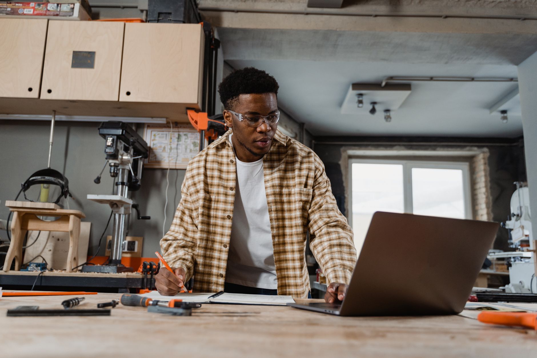 Carpenter using laptop and tools in a workshop, strategizing for a woodworking project.