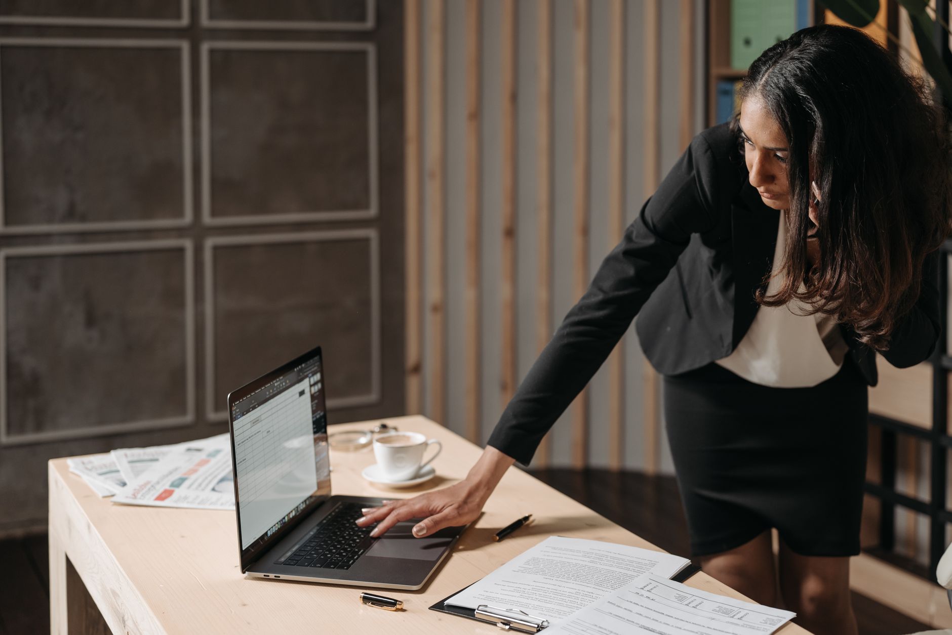 Professional businesswoman multitasking at an office desk, focused on her tasks with a laptop.