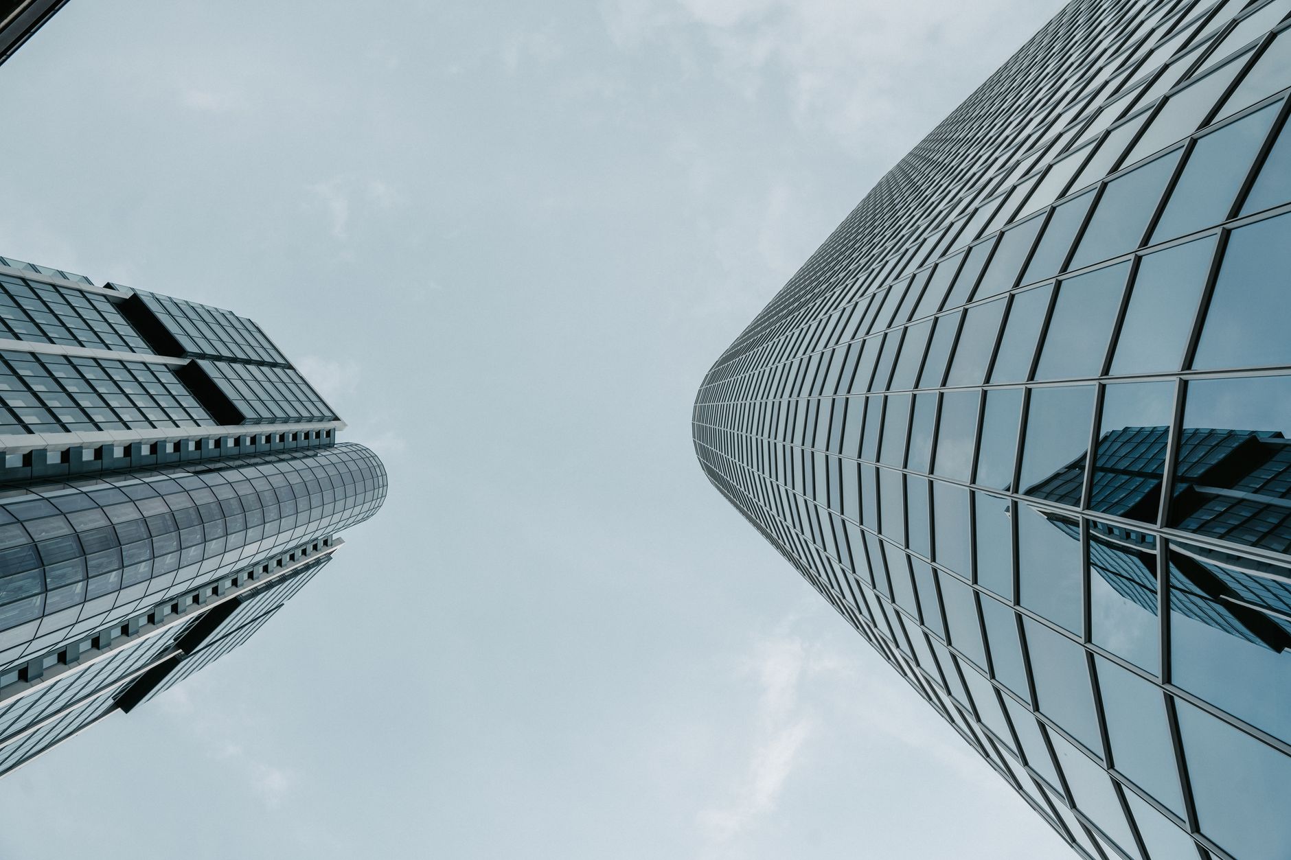 Low angle view of urban skyscrapers with reflective glass windows under a cloudy sky.