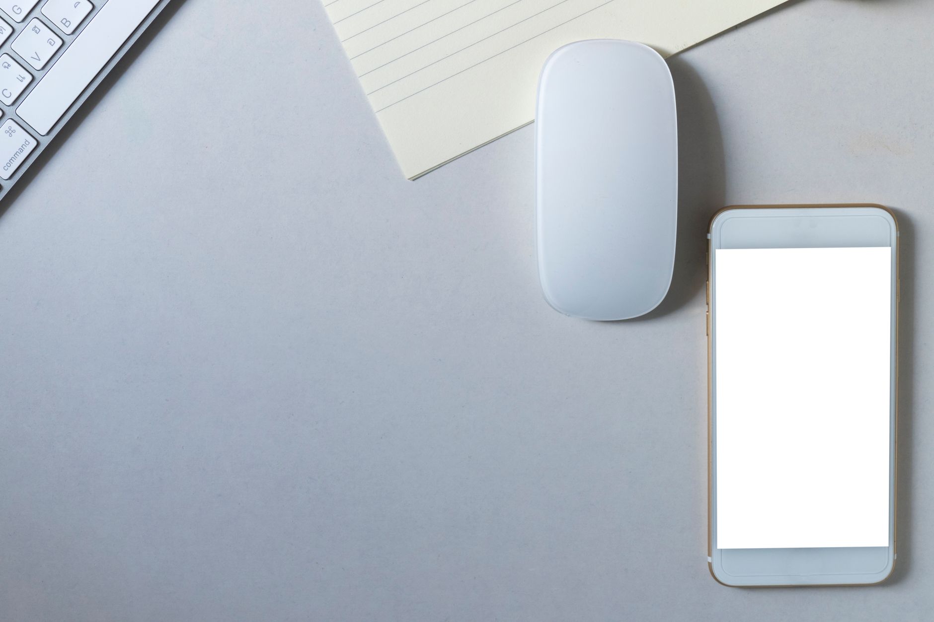 Contemporary workspace flat lay featuring a smartphone, wireless mouse, keyboard, and paper on a minimalist desk.