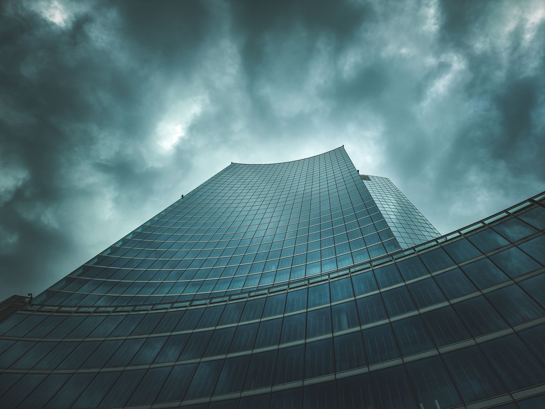Low-angle view of a sleek skyscraper against a dramatic cloudy sky, showcasing modern architecture.