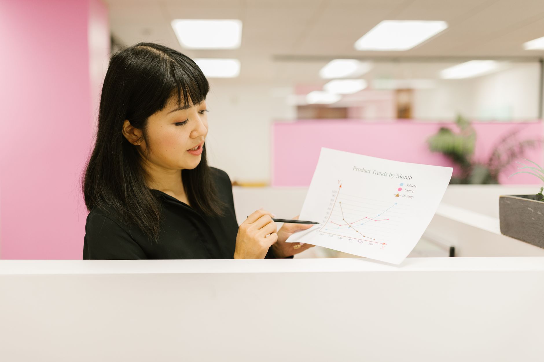 Asian woman presenting sales graph analysis in modern office setting.
