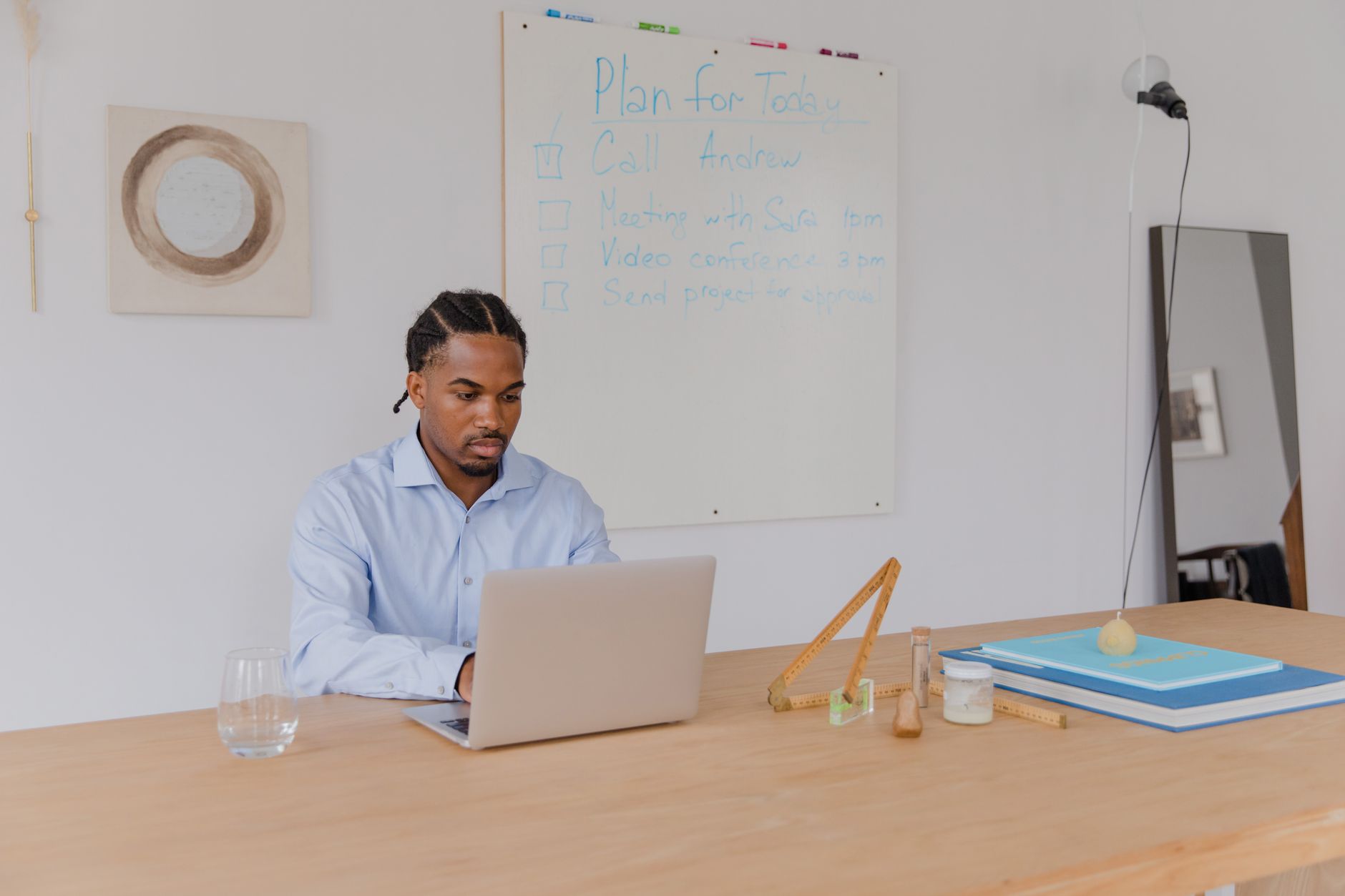 An adult man in a blue shirt working on a laptop in an office with a whiteboard.