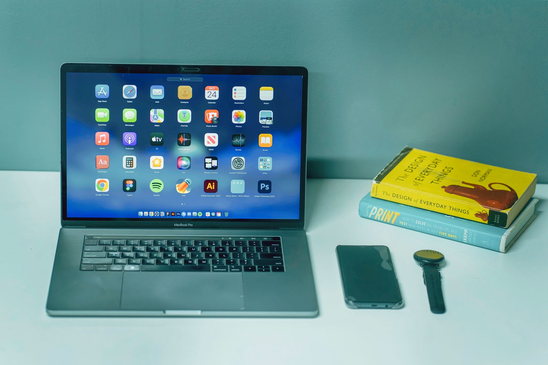 A sleek desk setup featuring a laptop, smartphone, watch, and books for a productive workspace.