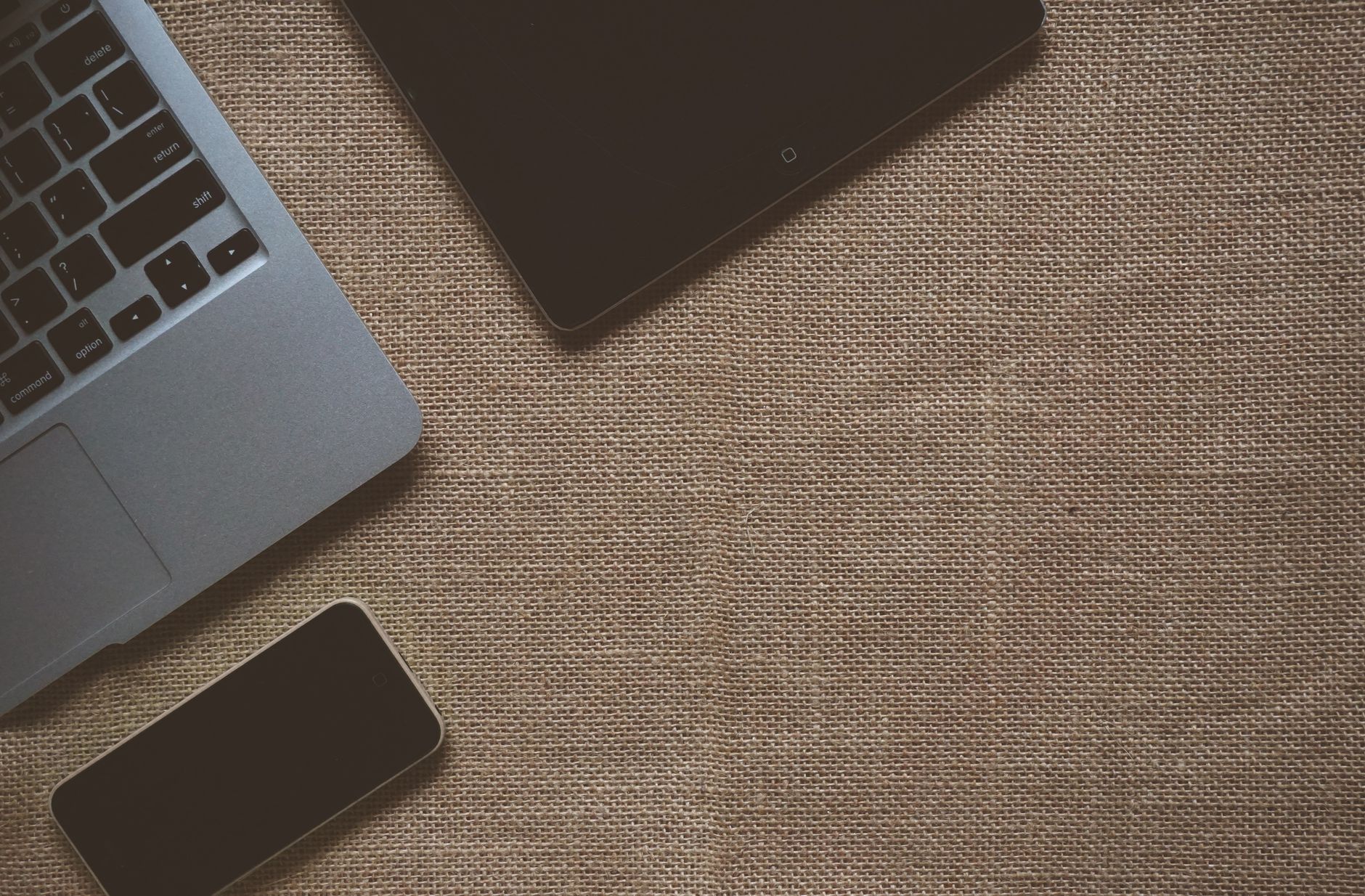 Flat lay image of laptop, tablet, and smartphone on a brown textured sackcloth surface.