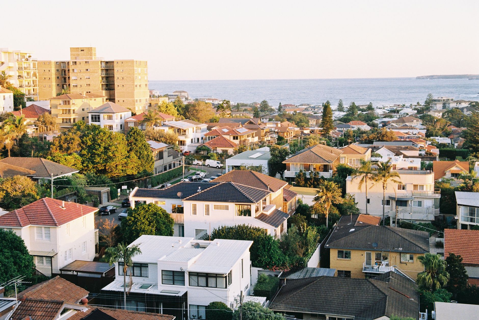 Aerial view of a coastal town with colorful houses and sea horizon at sunset.