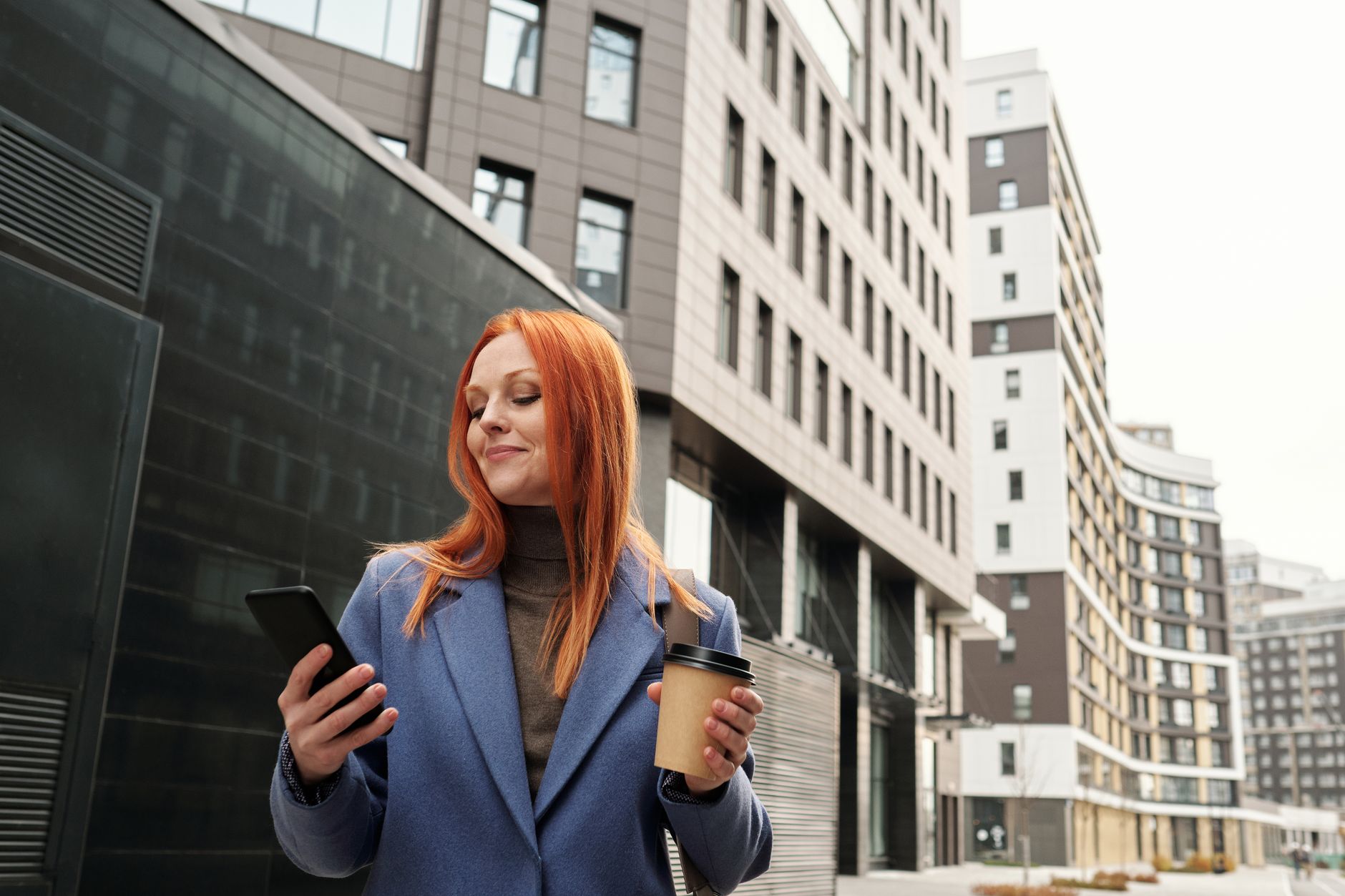 Confident businesswoman enjoying coffee while checking her smartphone in the city.