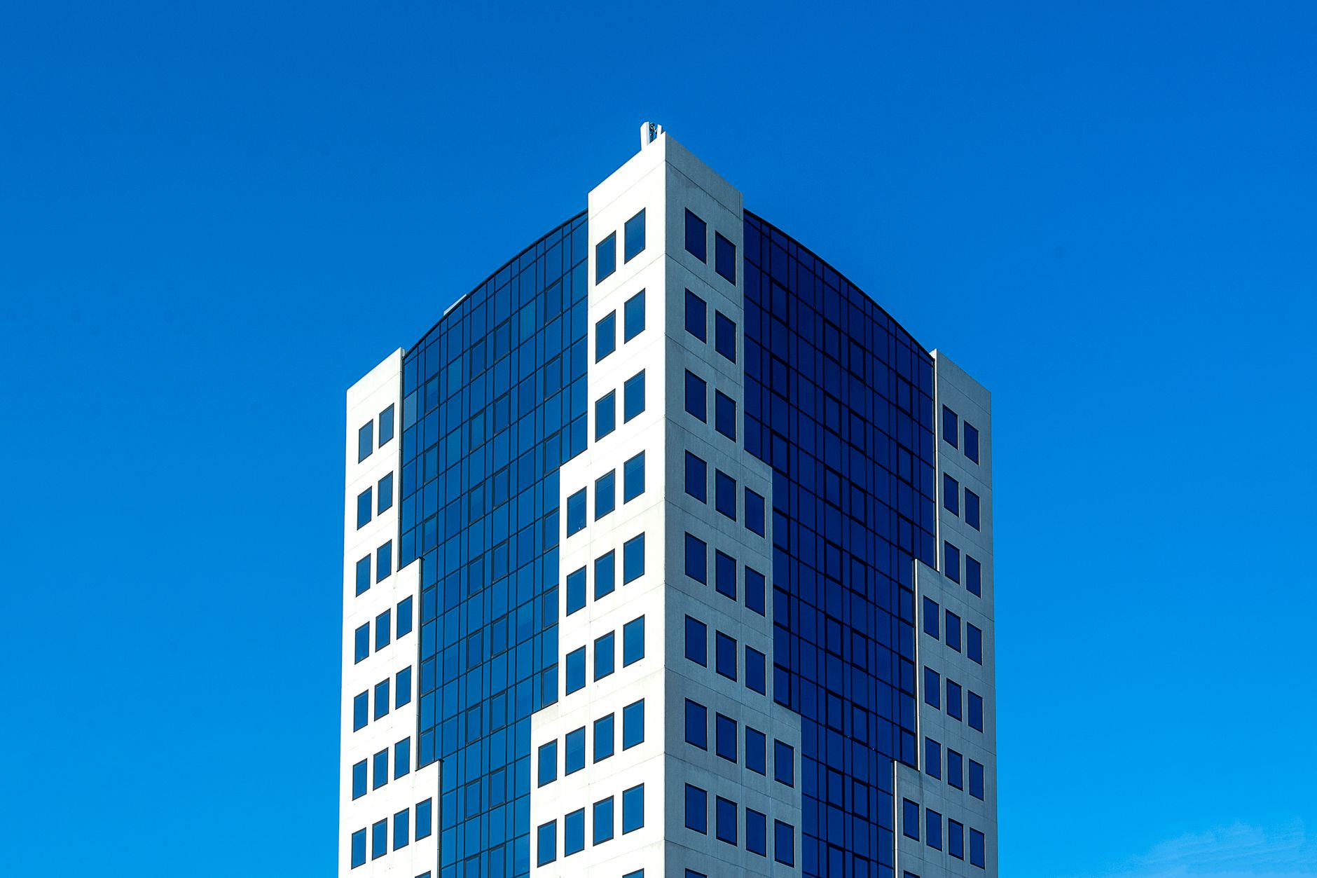 Modern high-rise office building with reflective windows set against a clear blue sky.