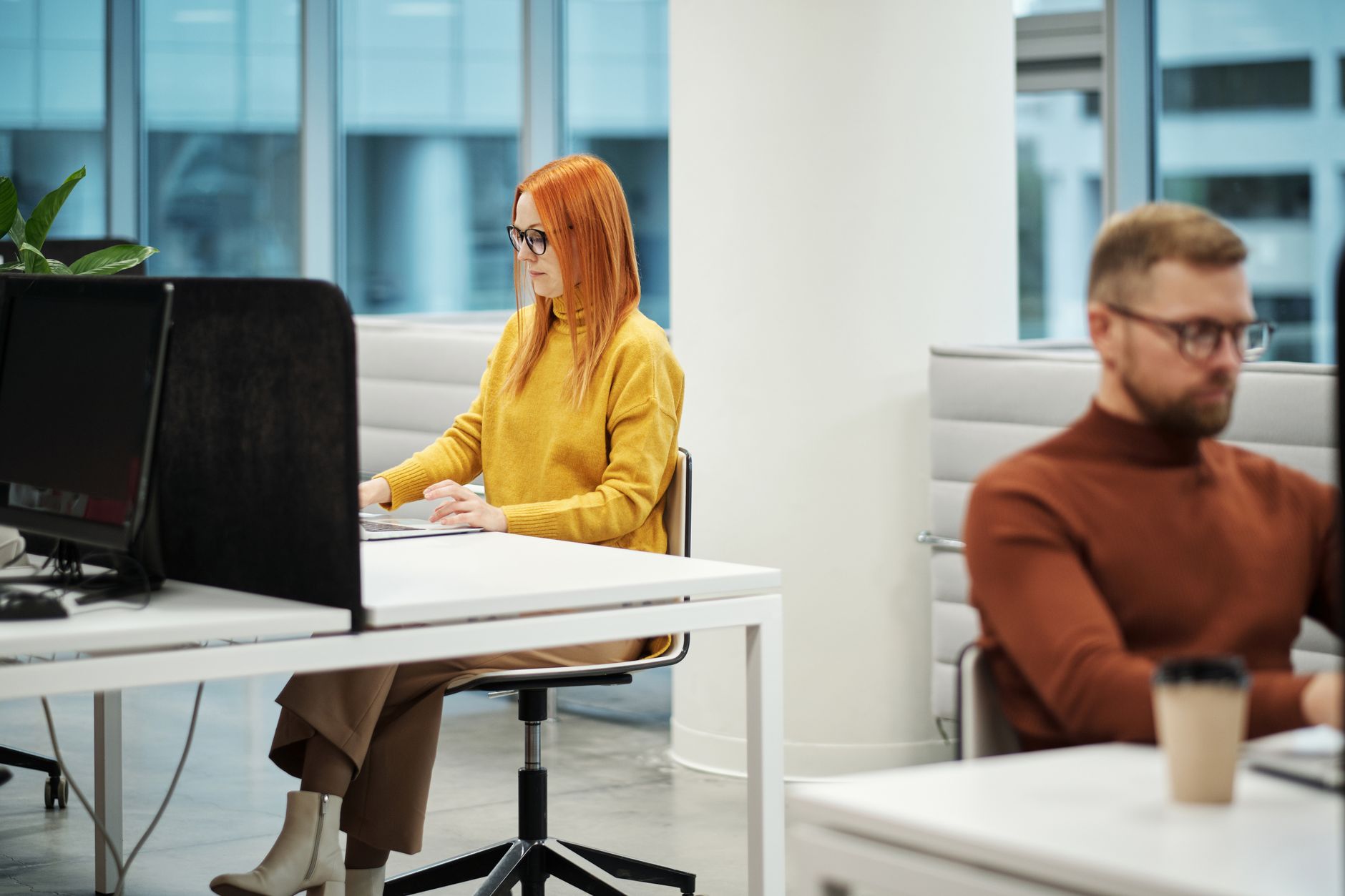 Two professionals working in a contemporary office environment with computers and casual attire.