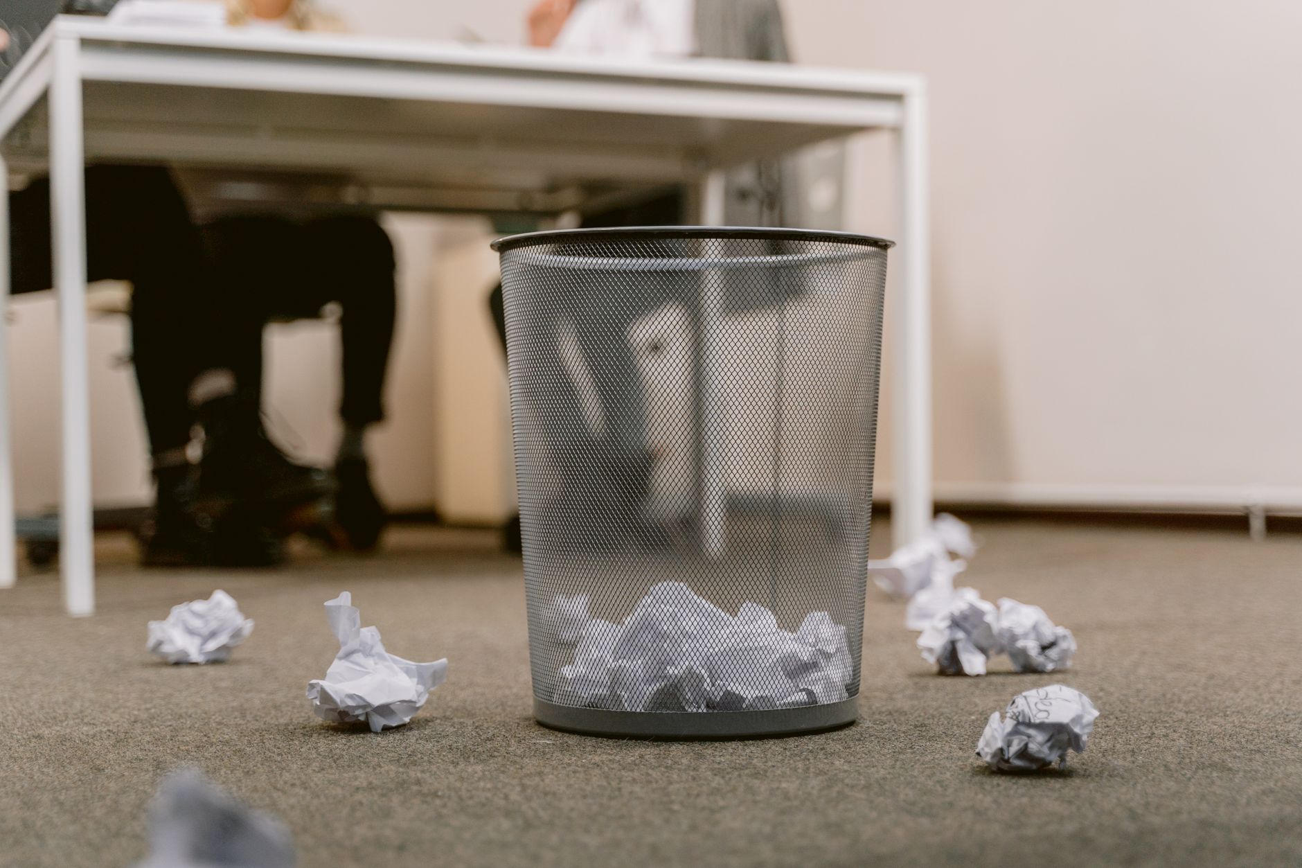 Office floor with a visible trash bin and crumpled papers scattered around, blurring human figures.