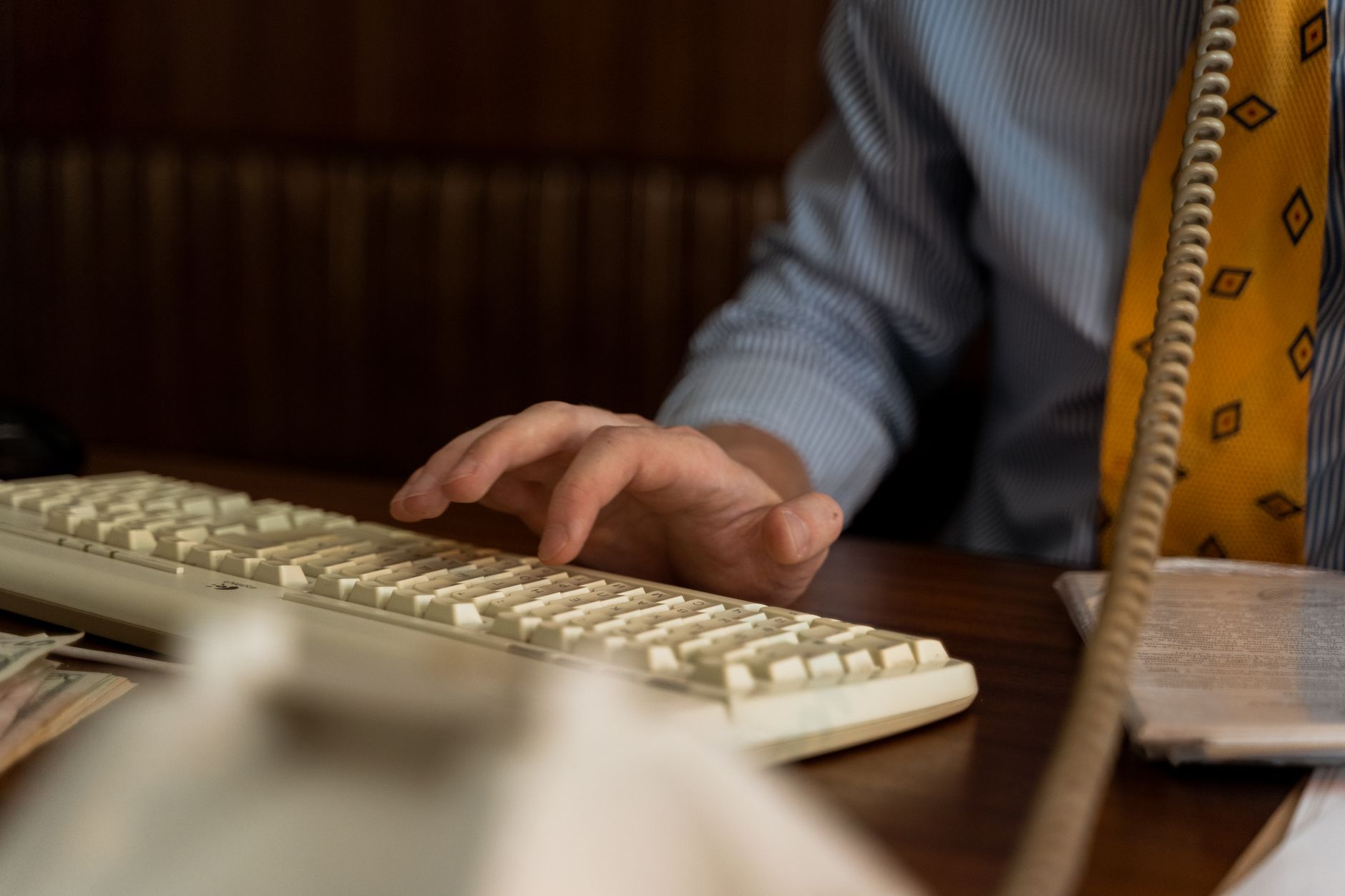 A close-up shot of a man typing on a vintage keyboard, dressed in business attire.