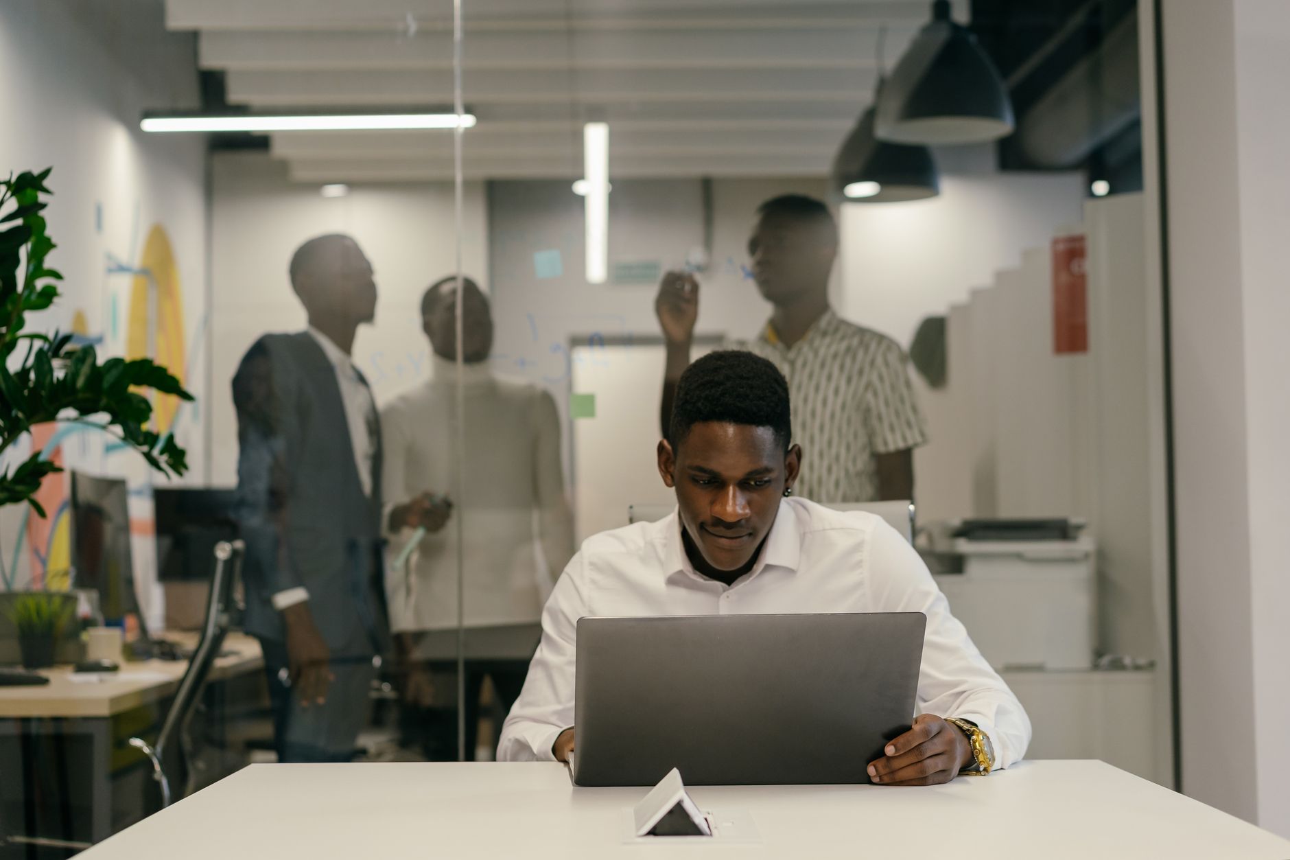A man in a white shirt works intently on a laptop at a modern office desk.