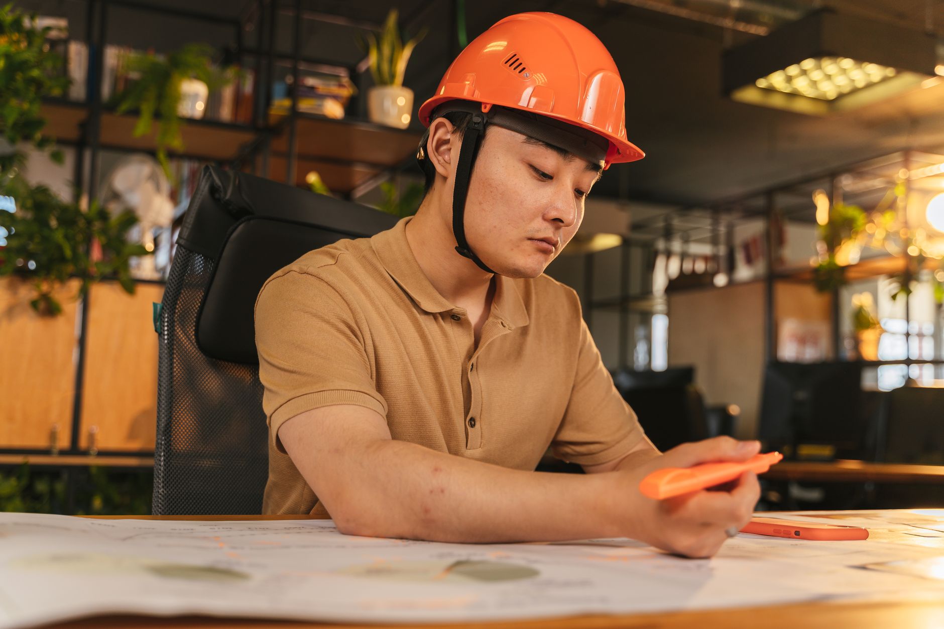 Young architect wearing helmet working on blueprint in modern office.