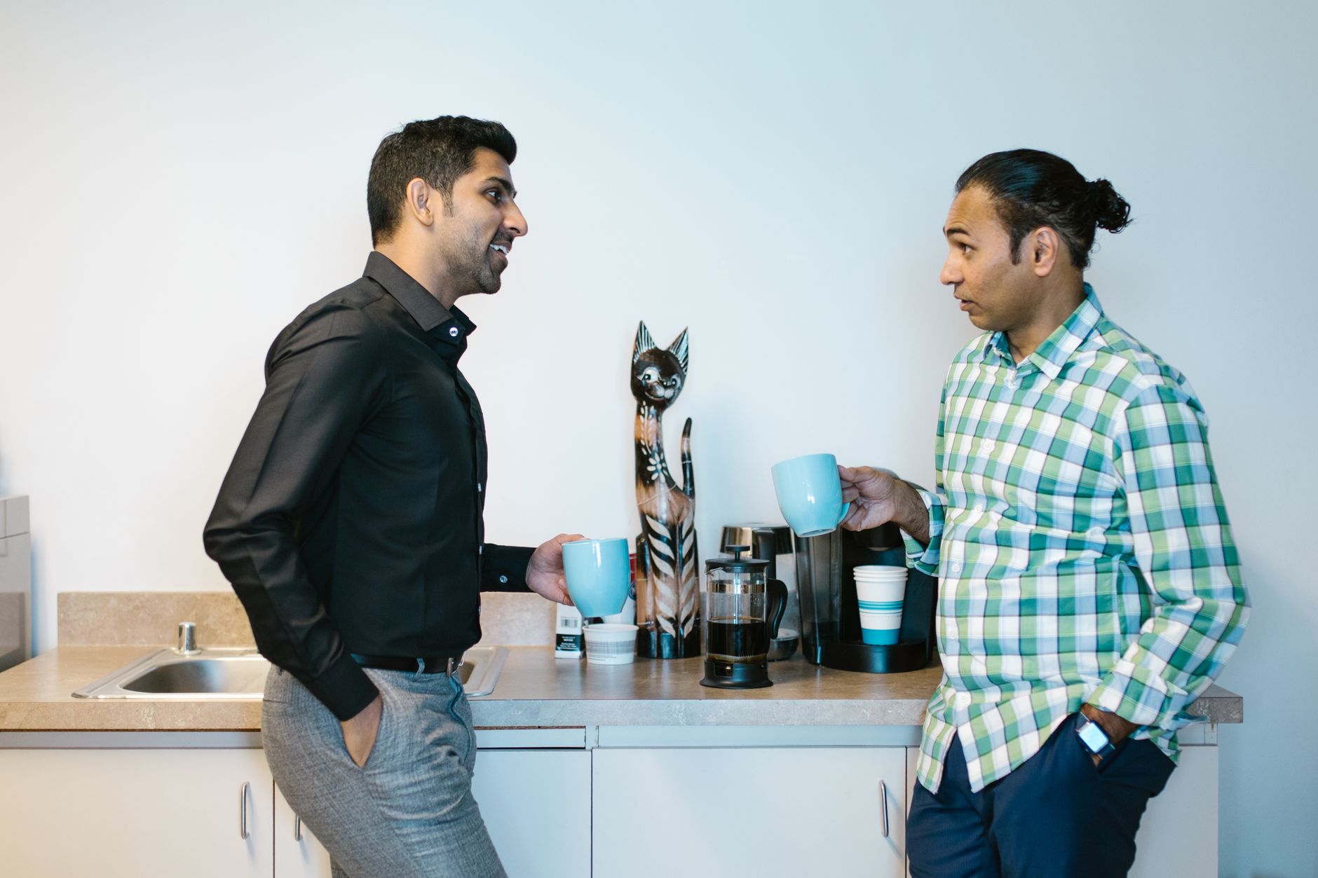 Two colleagues enjoy a coffee break in a modern office kitchen setting.