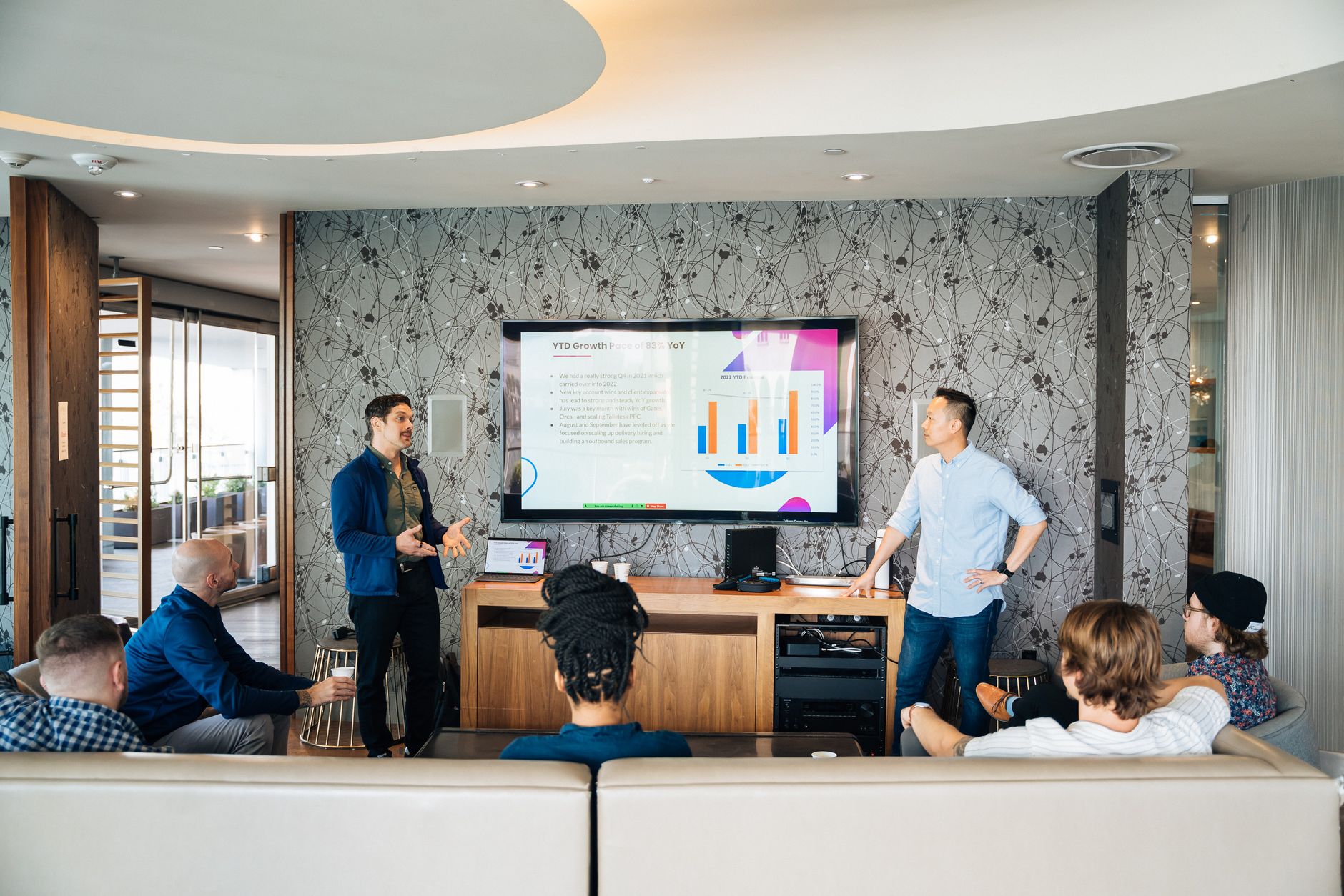 Group of professionals engaging in a business presentation with a TV displaying graphs.
