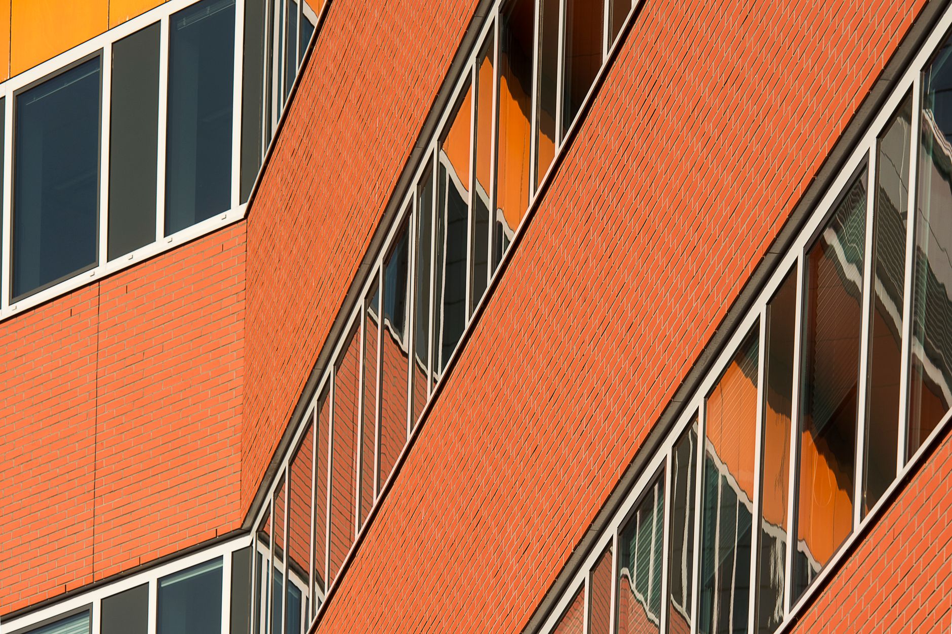 Close-up of modern architectural facade with orange brickwork and reflective windows.