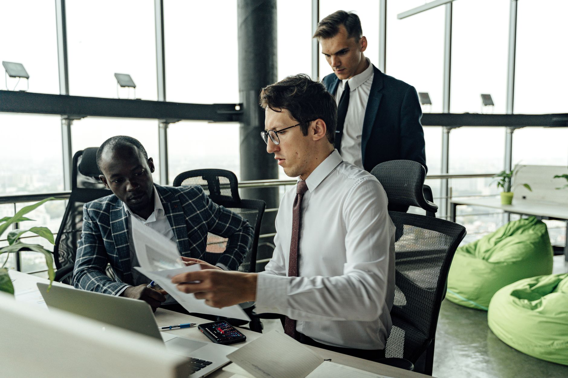Professionals engaging in teamwork and discussion in a contemporary office setting with large windows.