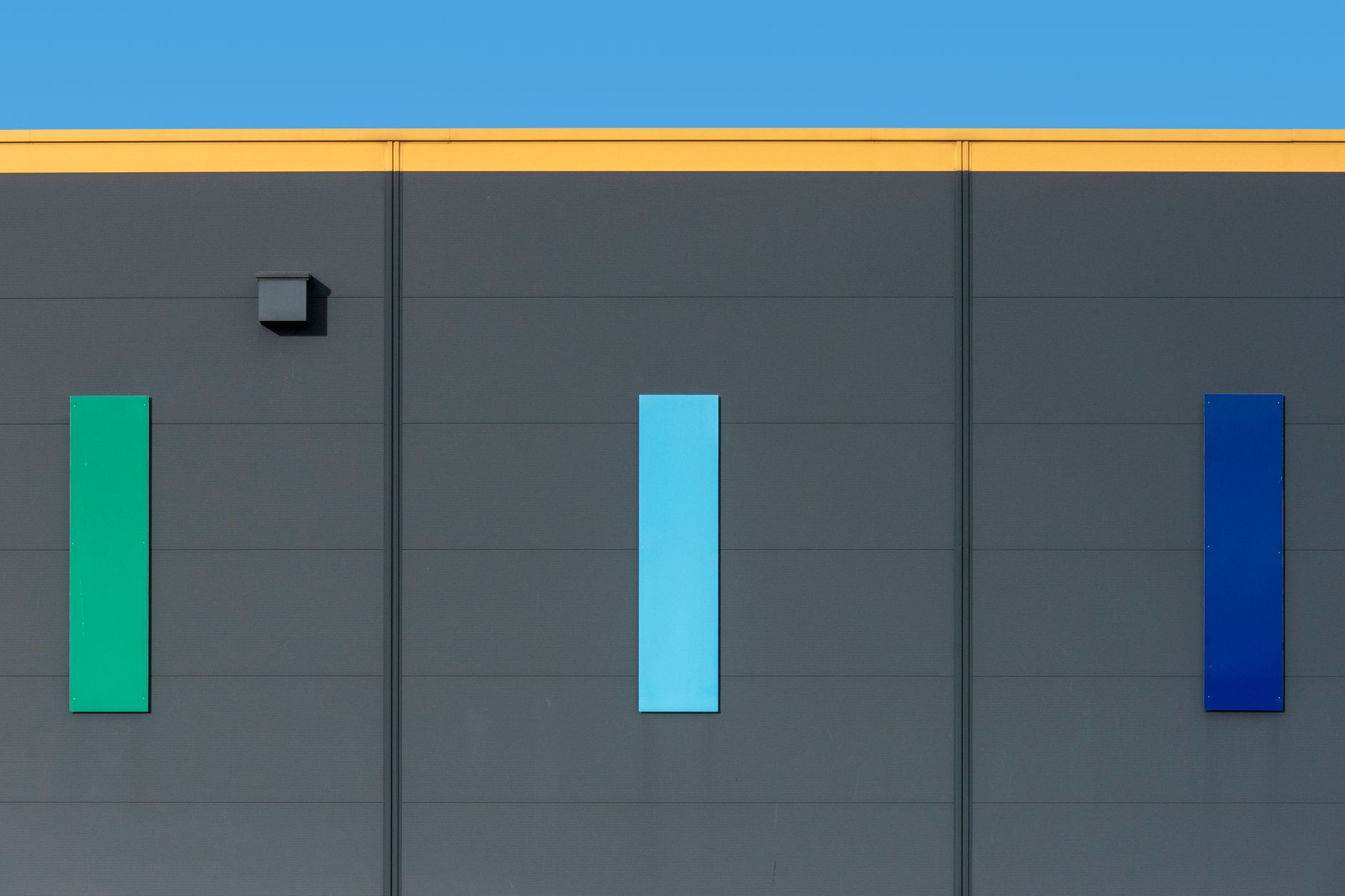 Modern facade with colorful panels against clear blue sky. Minimalist architecture.